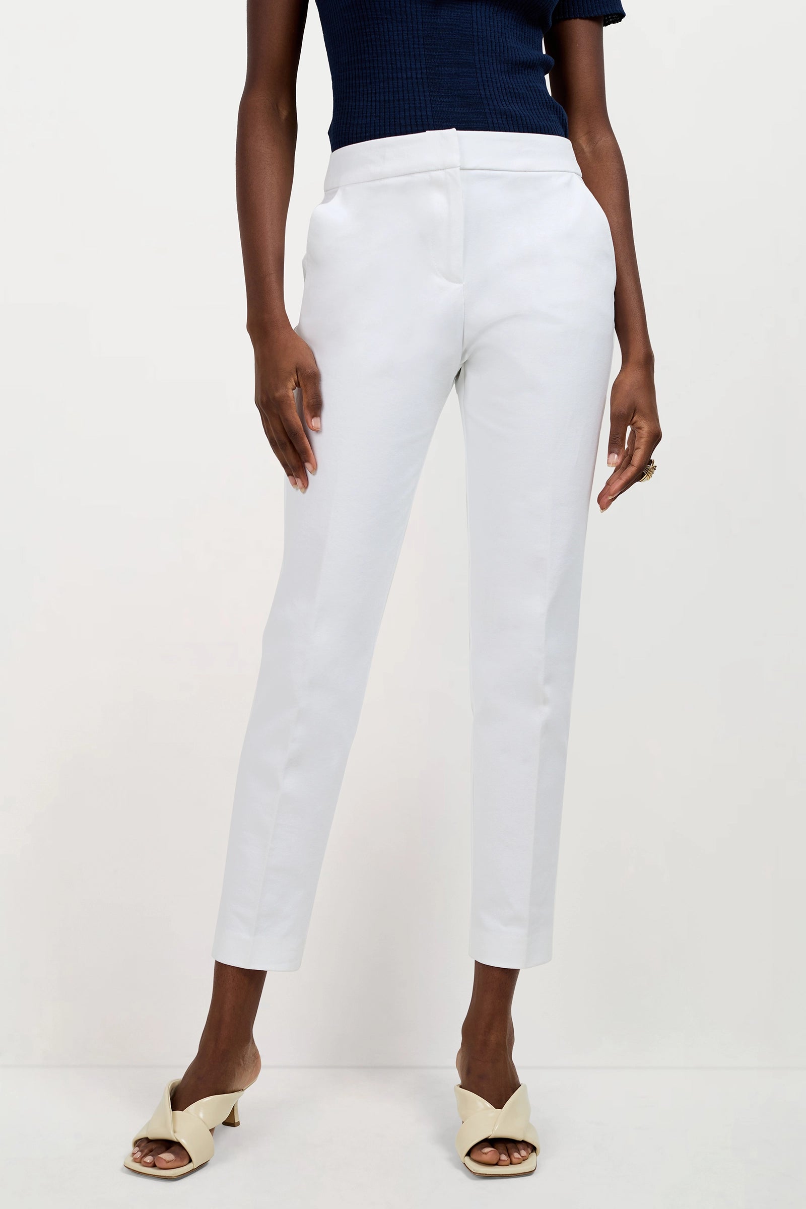 Wearing the Aubree 2 Cigarette Pants in white, paired with a navy top and cream heeled sandals, a model stands against a plain light background. The shoulder-down photo highlights the chic ankle-length tailored pants.