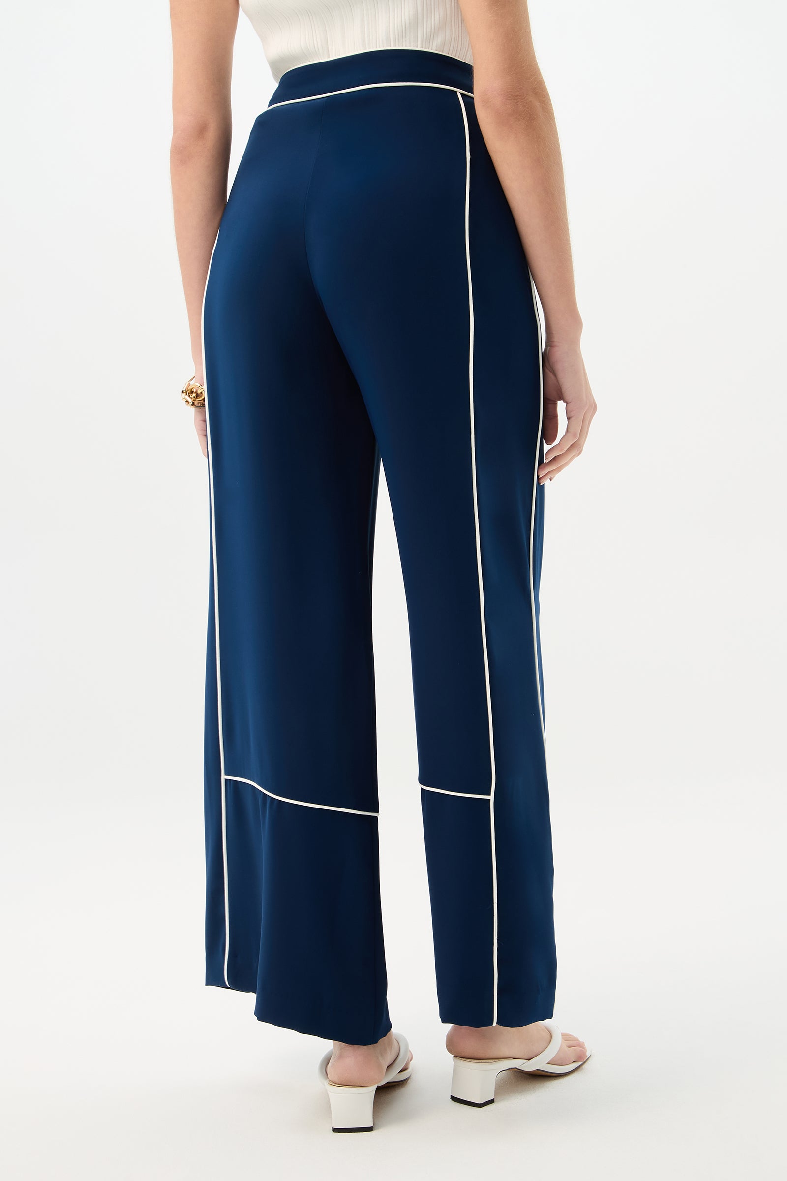 A person is shown from the back on a white background, wearing Rivals Wide-Leg Pant - Double Georgette in navy with white piping, a sleeveless white top, white heeled sandals, and a gold bracelet.