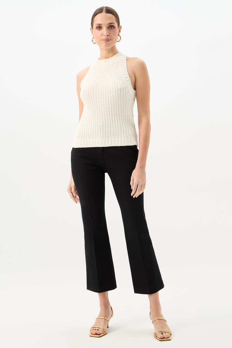 A woman stands against a white background wearing a sleeveless, ribbed cream knit top, beige heeled sandals, hoop earrings, and the Lulu Cropped Pant - Cotton Bi-Stretch in black; her hair is pulled back.