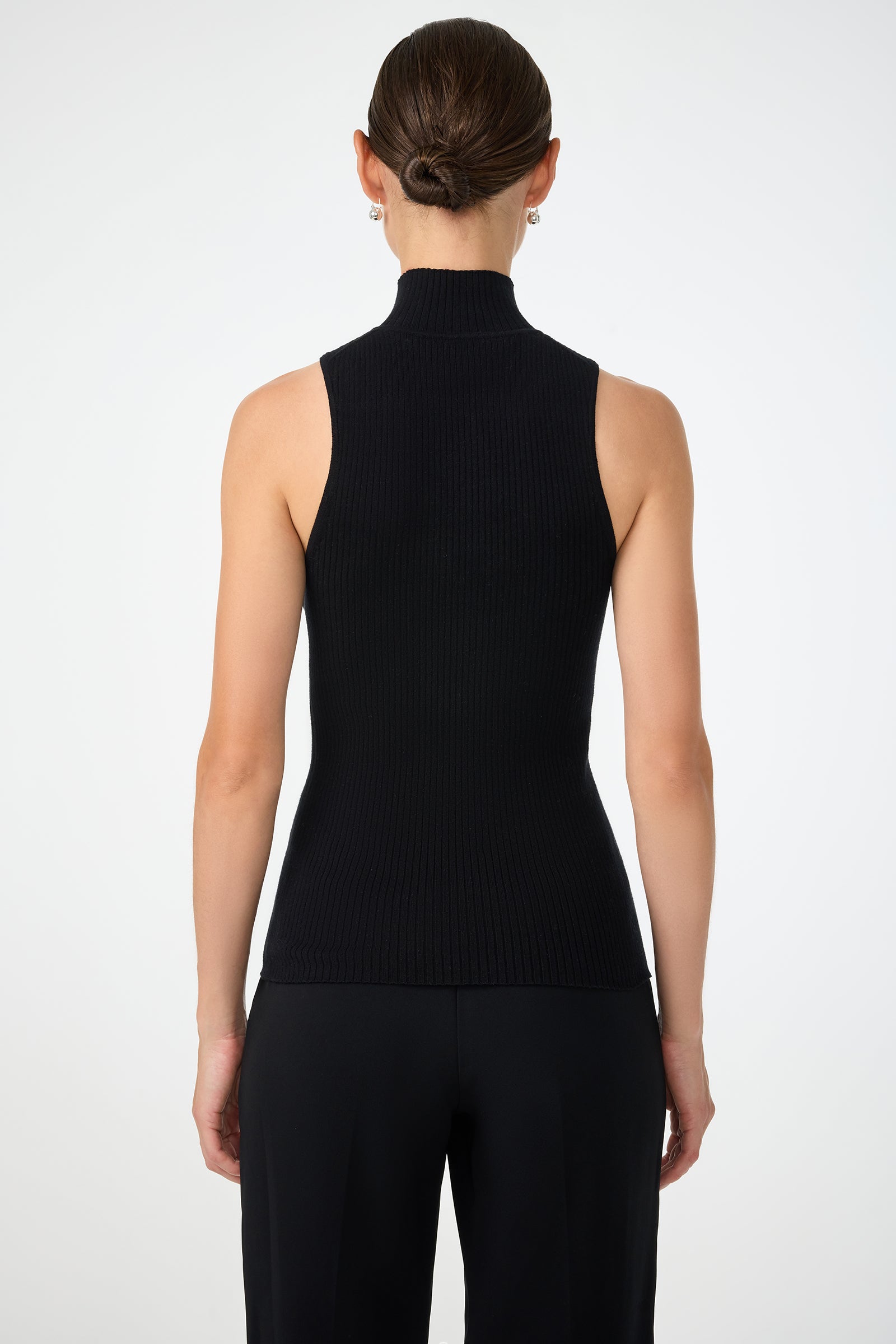 A woman with her hair tied back is shown from behind wearing the Westhampton Knit Pullover, a sleeveless black turtleneck top, and black pants against a plain white background.