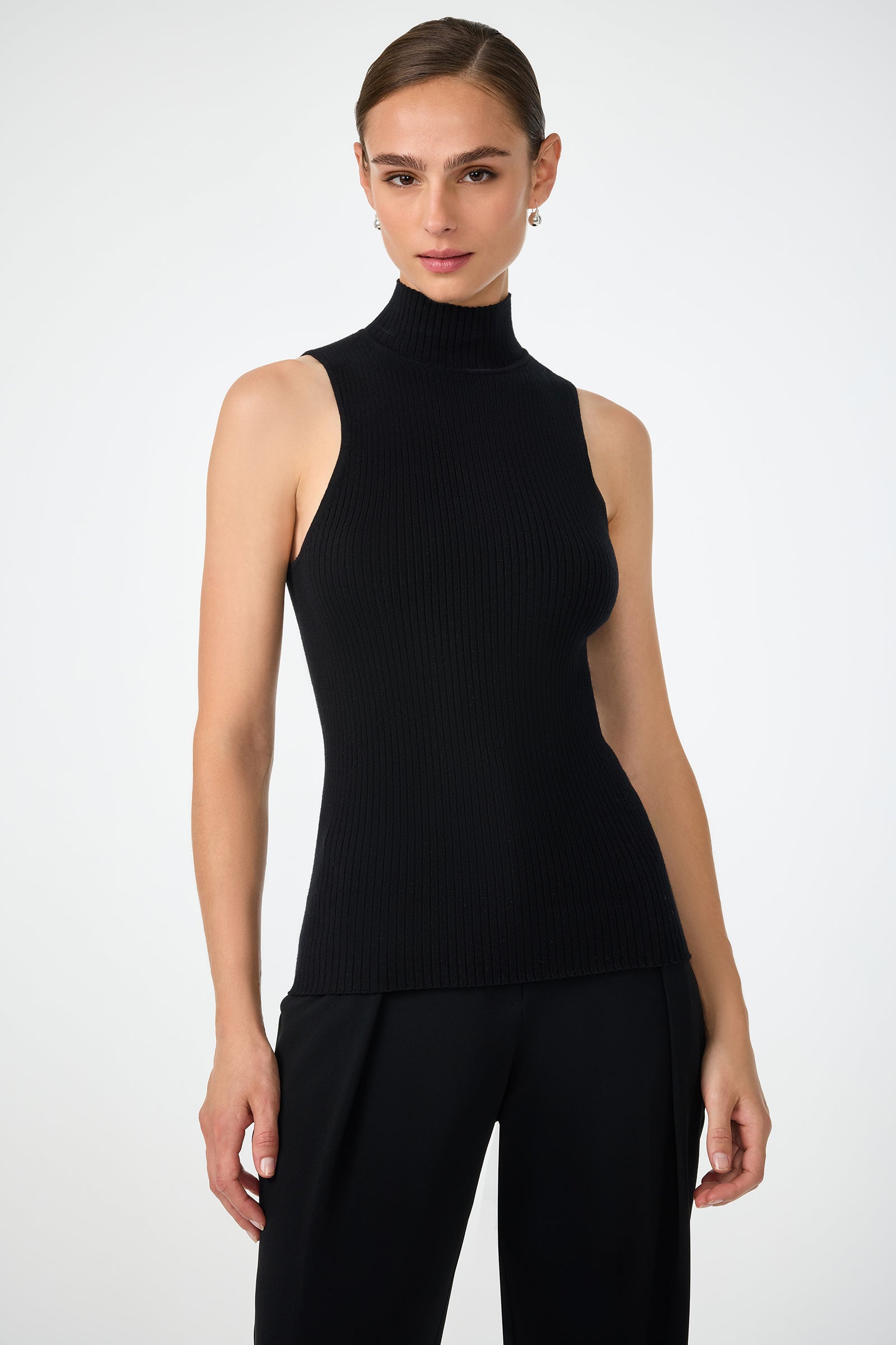 A woman with brown hair tied back wears the black Westhampton Knit Pullover with black pants, standing against a plain white background.