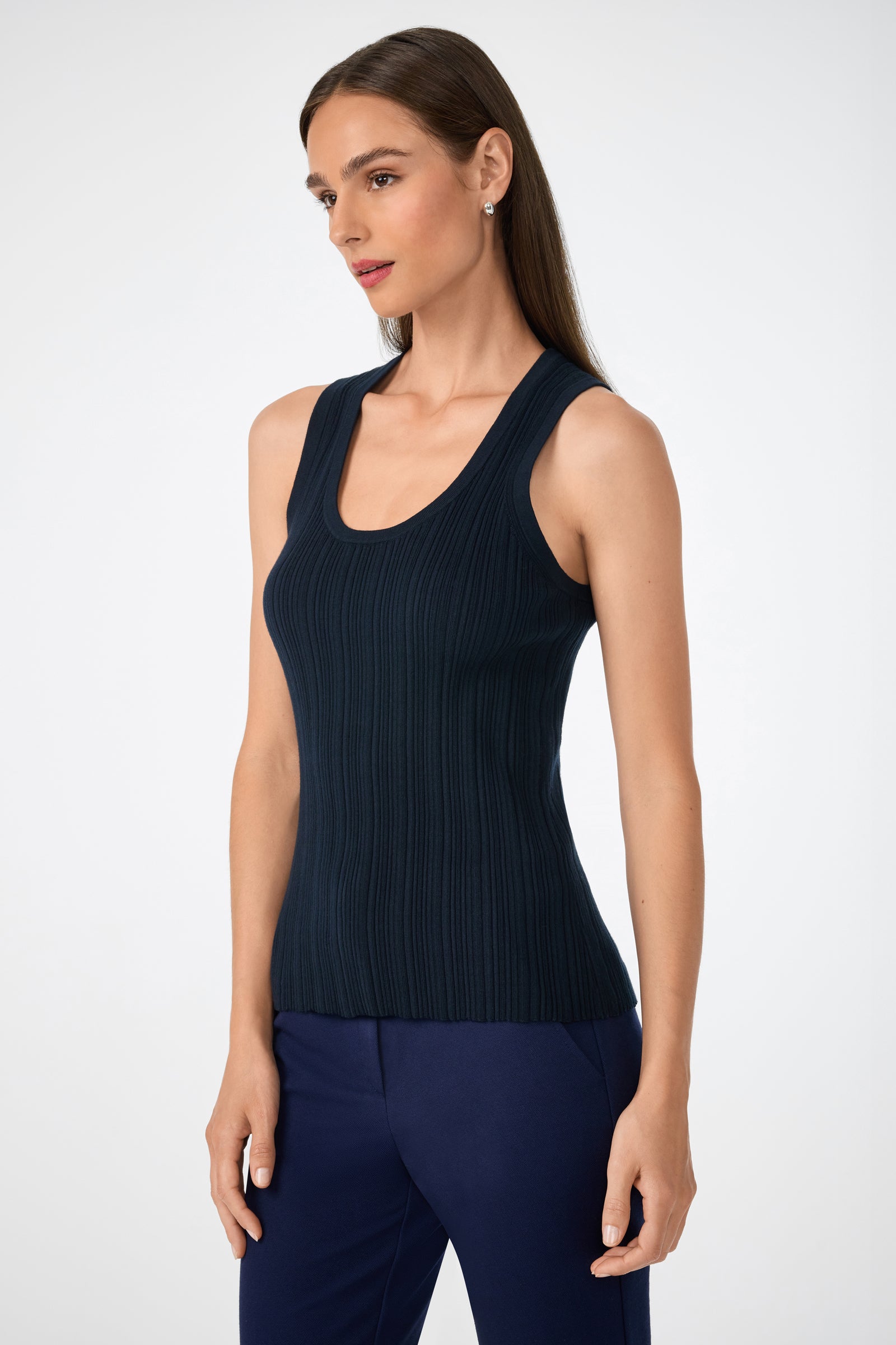 A woman with long brown hair wears the sleeveless Gibraltar Tank in dark navy with matching pants, standing against a plain white background and looking slightly to the side.