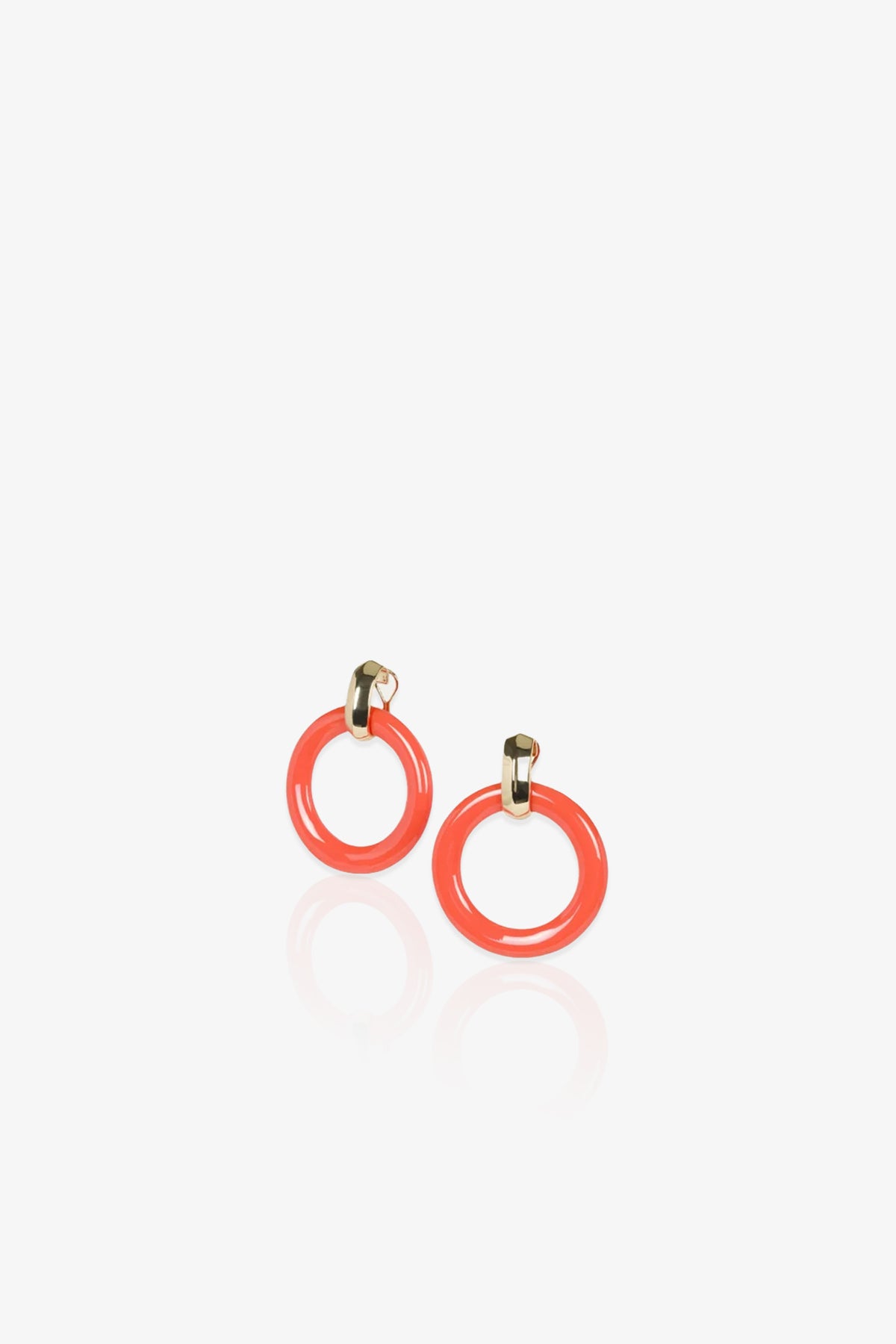 The TT x KJL Doorknocker Earrings in Coral feature glossy, coral-colored circular hoops accented with gold-tone studs, showcased on a white background with a subtle reflection beneath them.
