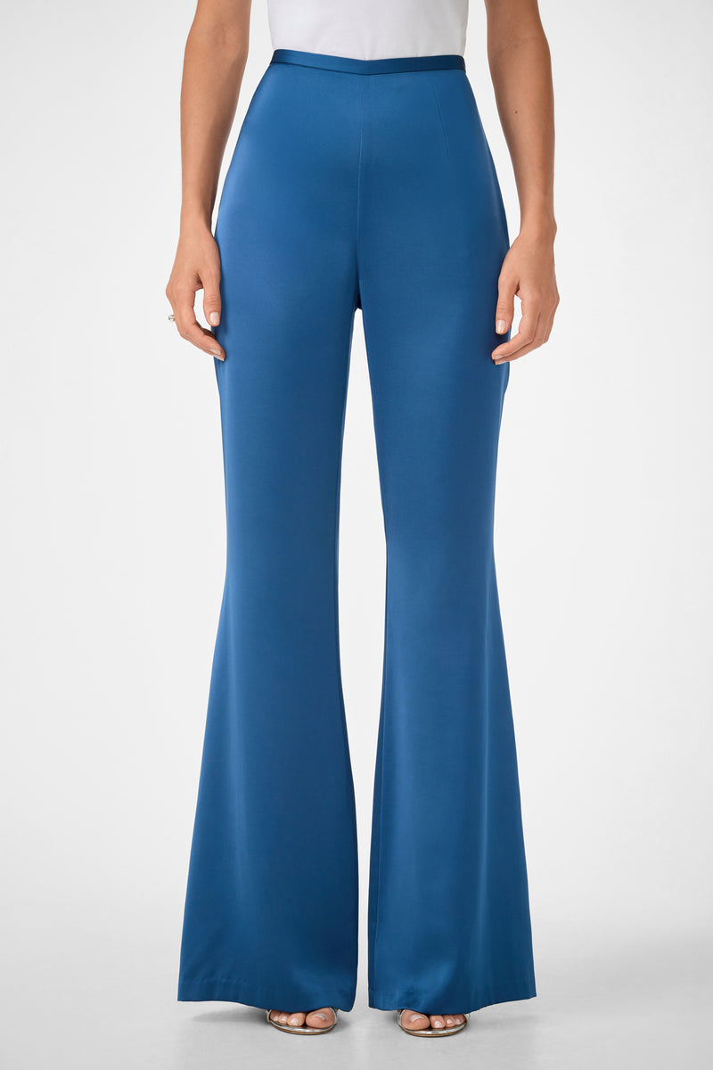 Woman wears Anmitsu Flared Pants in Sumi Blue, featuring a high waist and wide-leg fit, paired with a white top, standing against a plain light background.