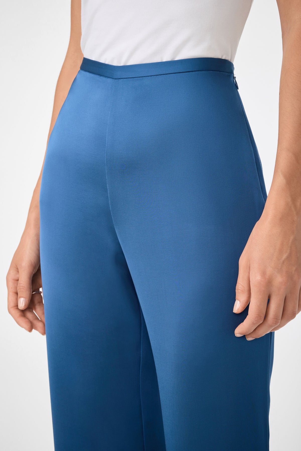 A person wearing Anmitsu Flared Pants—high-waisted, wide-leg blue trousers—paired with a tucked-in white top, shown from waist to mid-thigh with arms relaxed at their sides.