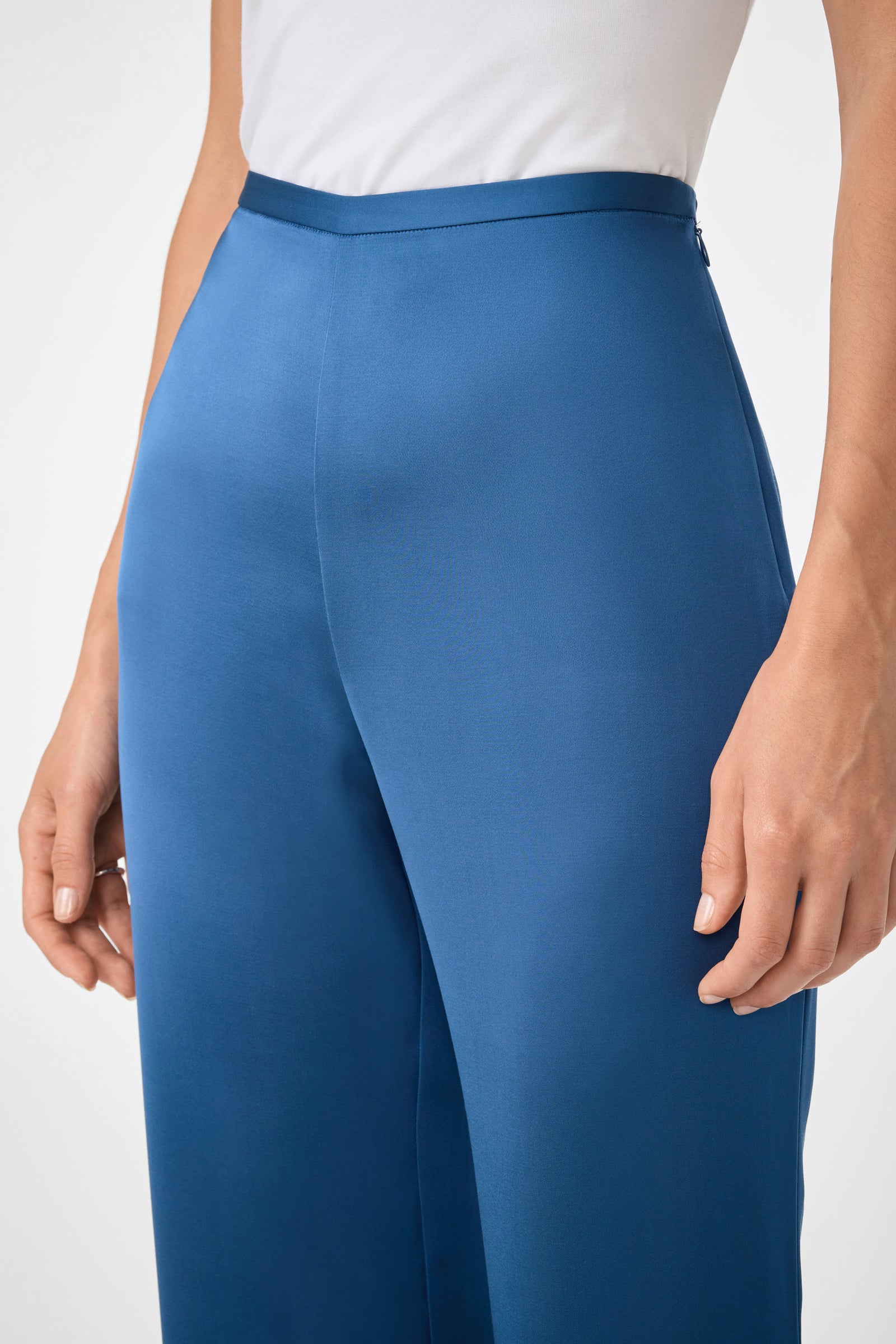 A person wearing Anmitsu Flared Pants—high-waisted, wide-leg blue trousers—paired with a tucked-in white top, shown from waist to mid-thigh with arms relaxed at their sides.