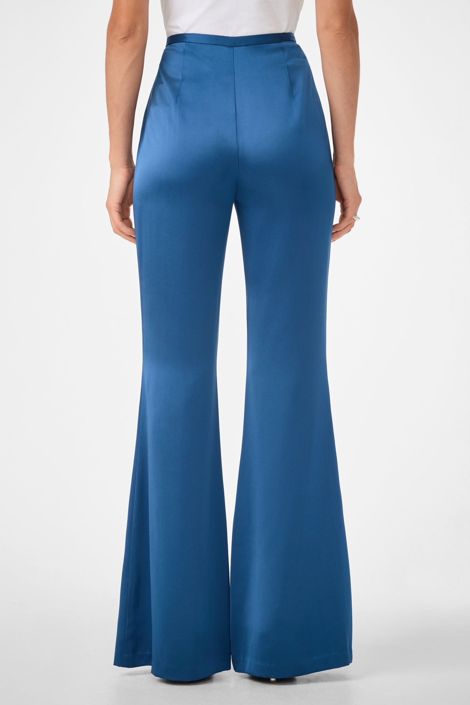A person is shown from the back, standing against a plain white background, wearing Anmitsu Flared Pants in blue with a high-waisted, flared design and a white shirt.
