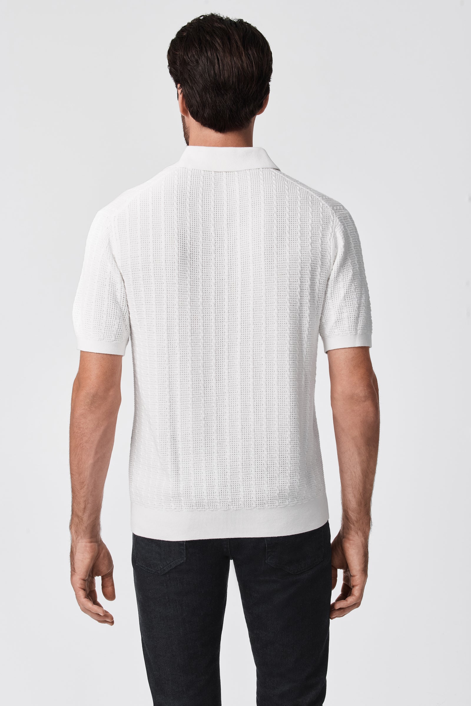 A man stands facing away, wearing the Asher Short-Sleeve Polo in textured white and black pants against a plain white background.