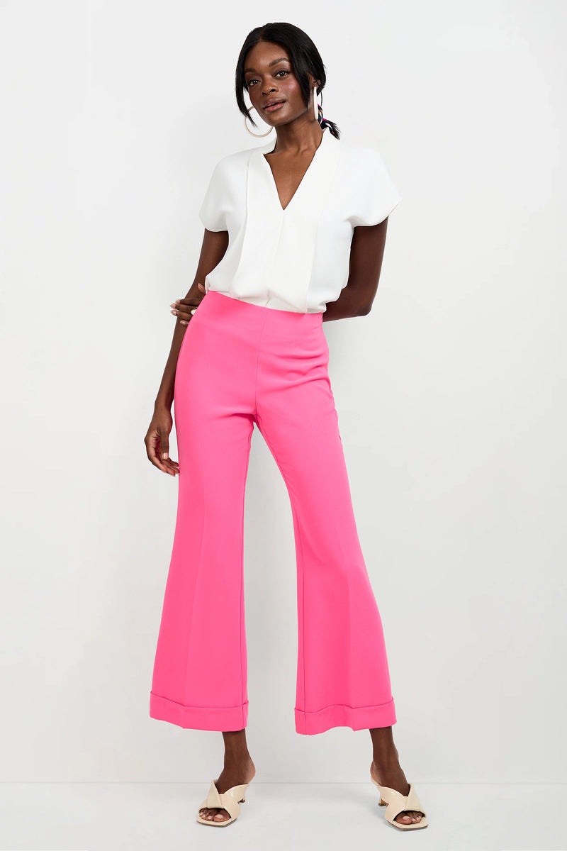 A woman poses against a white background wearing the Turin Slash Tie Top, bright pink high-waisted wide-leg pants, and cream open-toe heels. She smiles softly with one hand on her hip.