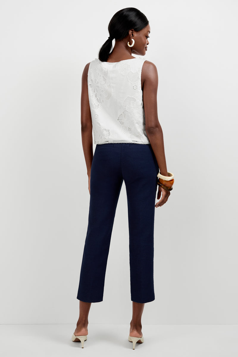 A woman faces away against a plain white background, wearing the Diffuse Pant in navy blue with a tulip hem, a sleeveless white lace top, cream low-heeled shoes, large hoop earrings, and chunky bracelets.