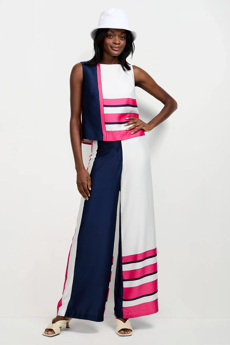 A woman in a white bucket hat wears the Cadorna Linee Sleeveless Top with wide-leg navy, white, and pink striped pants and open-toed heels, posing with one hand on her hip against a plain background.