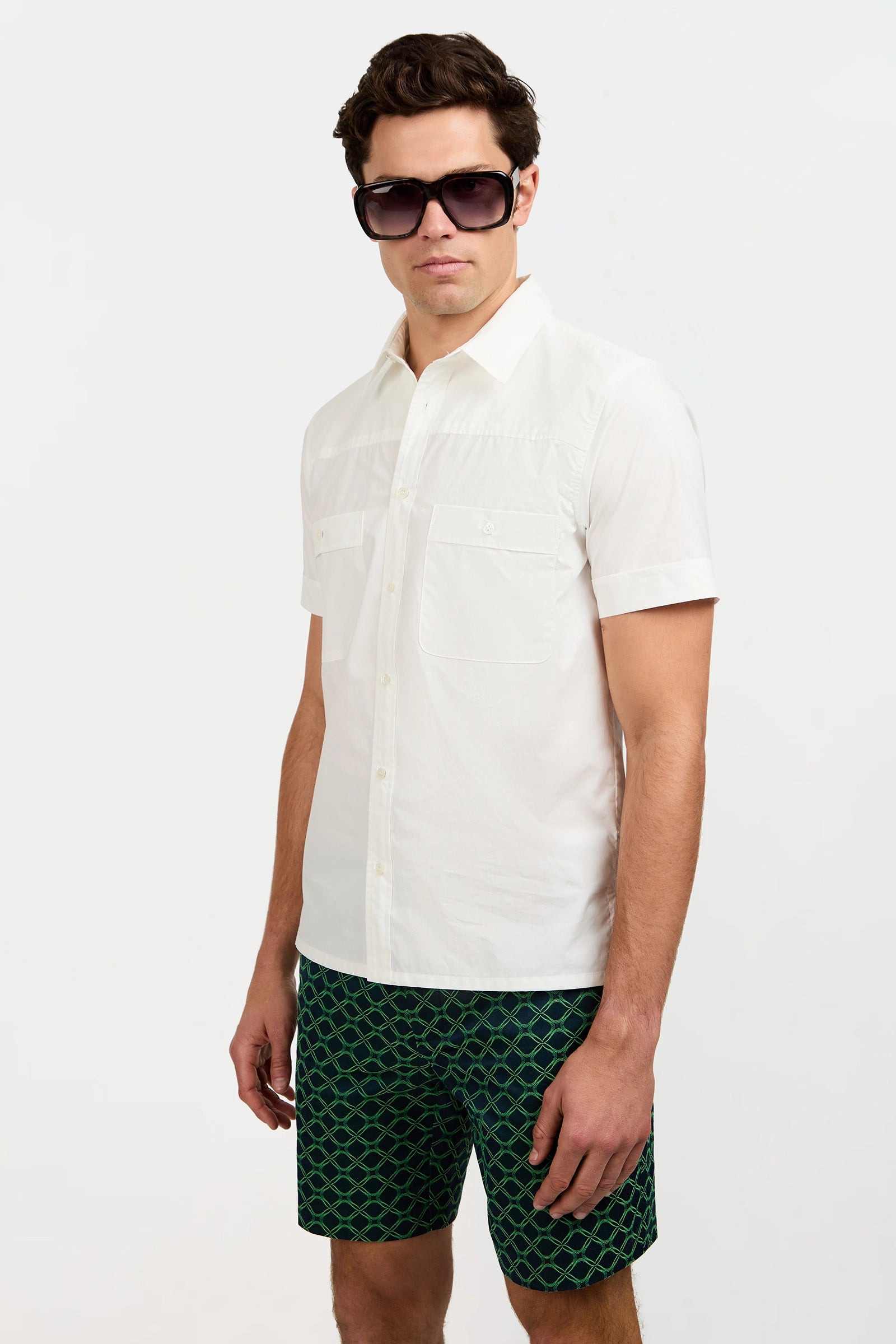 A man in the Will Short-Sleeve Shirt, large dark sunglasses, and green patterned shorts stands against a plain white background.