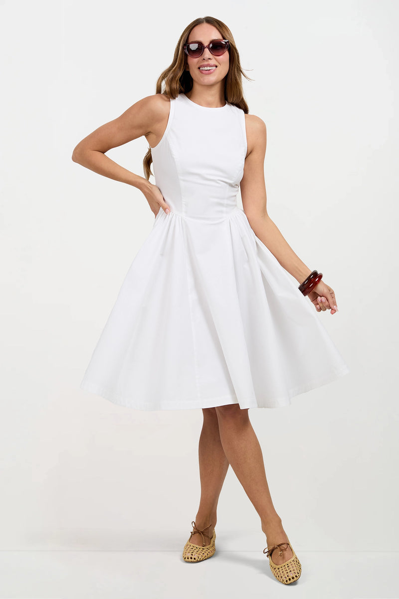A woman smiles in the sleeveless white Lombardy Midi Dress, tan woven flats, brown bracelets, and sunglasses, posing with one hand on her hip and the other holding her skirt.