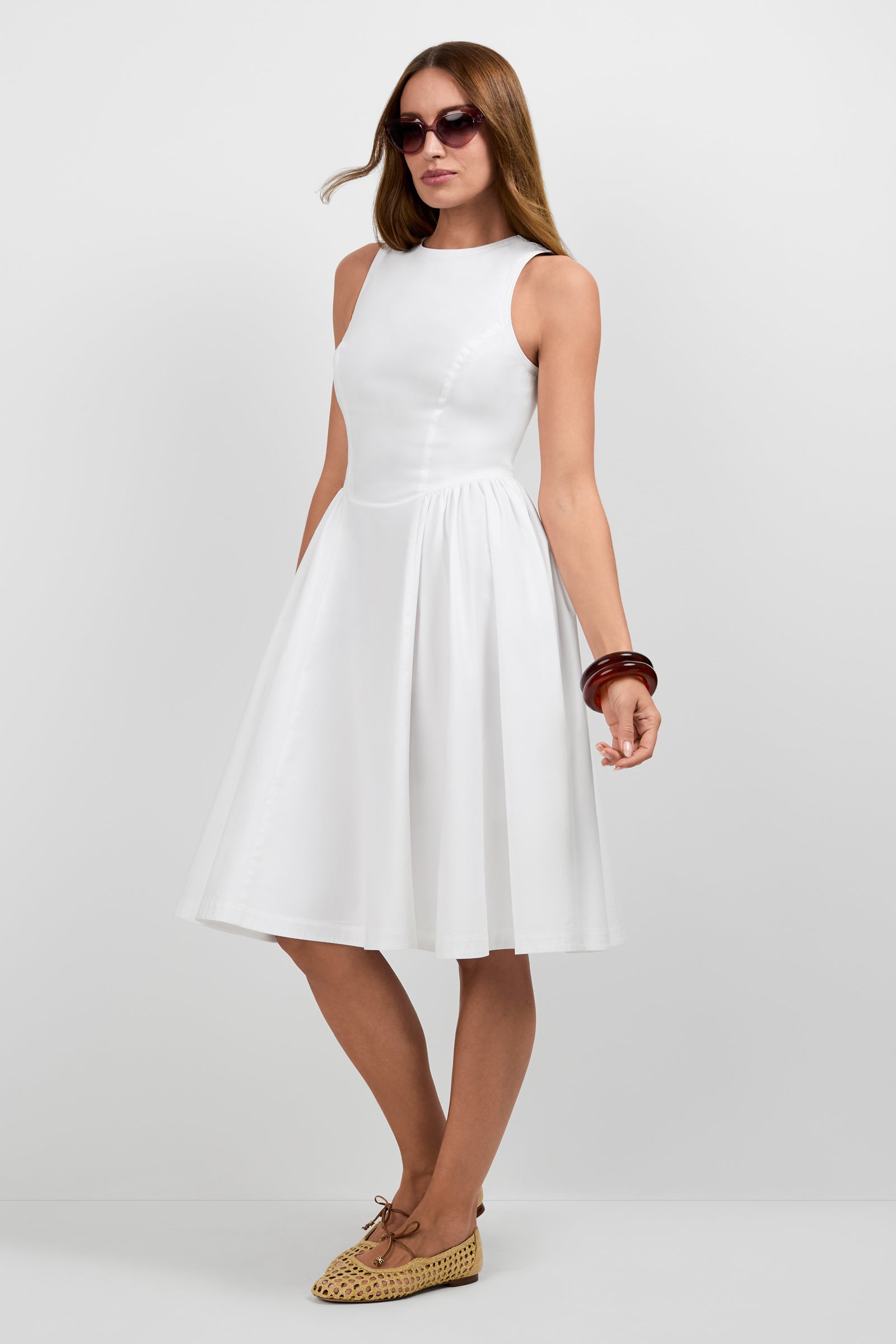 A woman wearing the Lombardy Midi Dress, brown sunglasses, woven flat shoes, and chunky brown bracelets stands against a plain white background.