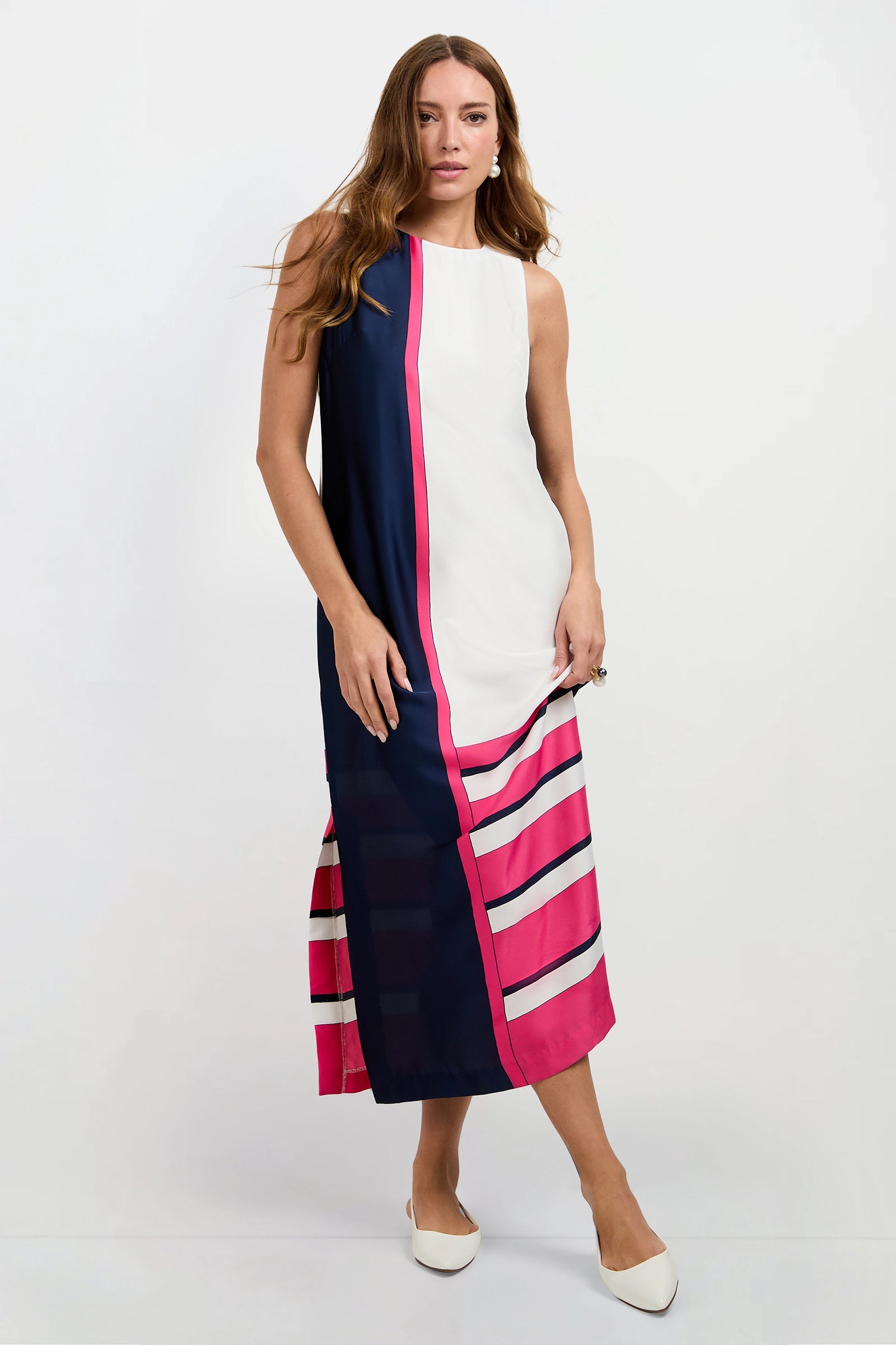 A woman models the Moderna Linee Midi Dress—a sleeveless, ankle-length style with navy sides, a white center, and pink striped accents—paired with white pointed-toe flats against a plain white background.