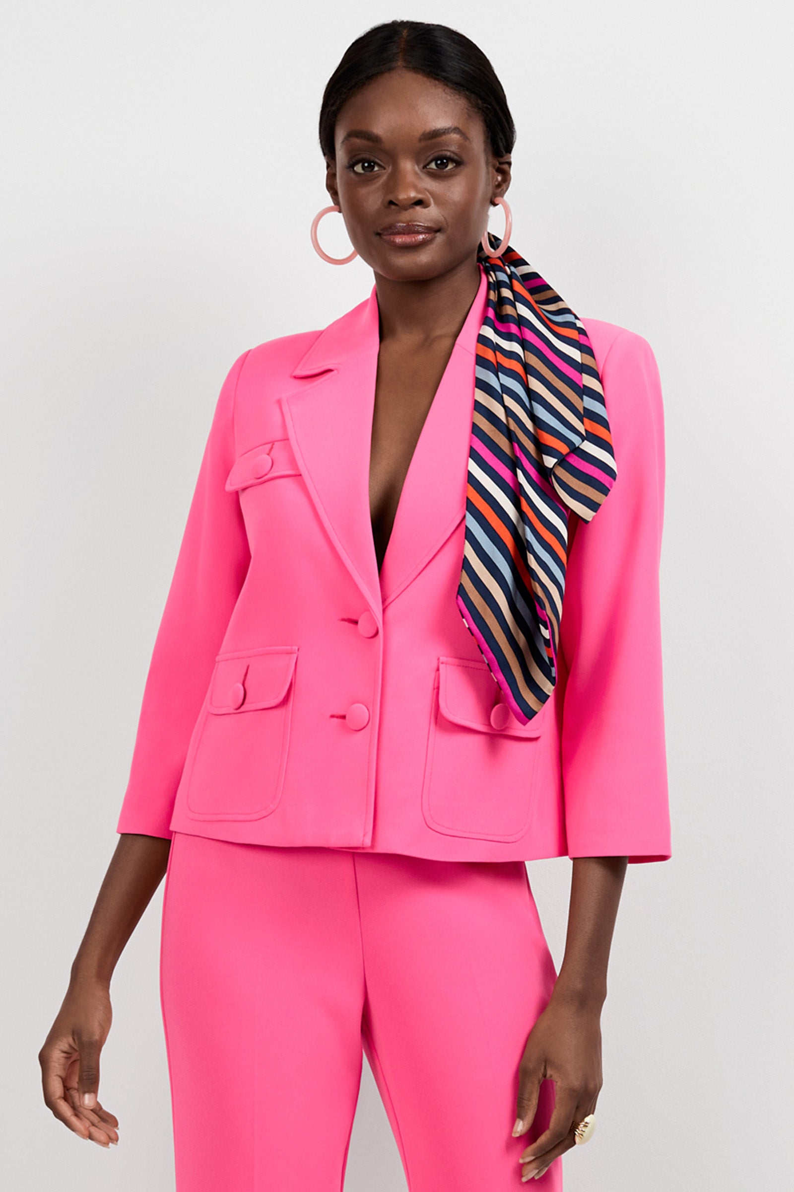 A woman stands confidently in the Bicocca Patch Pocket Jacket and matching pants, accented by hoop earrings and a striped scarf in her hair, set against a plain light background.