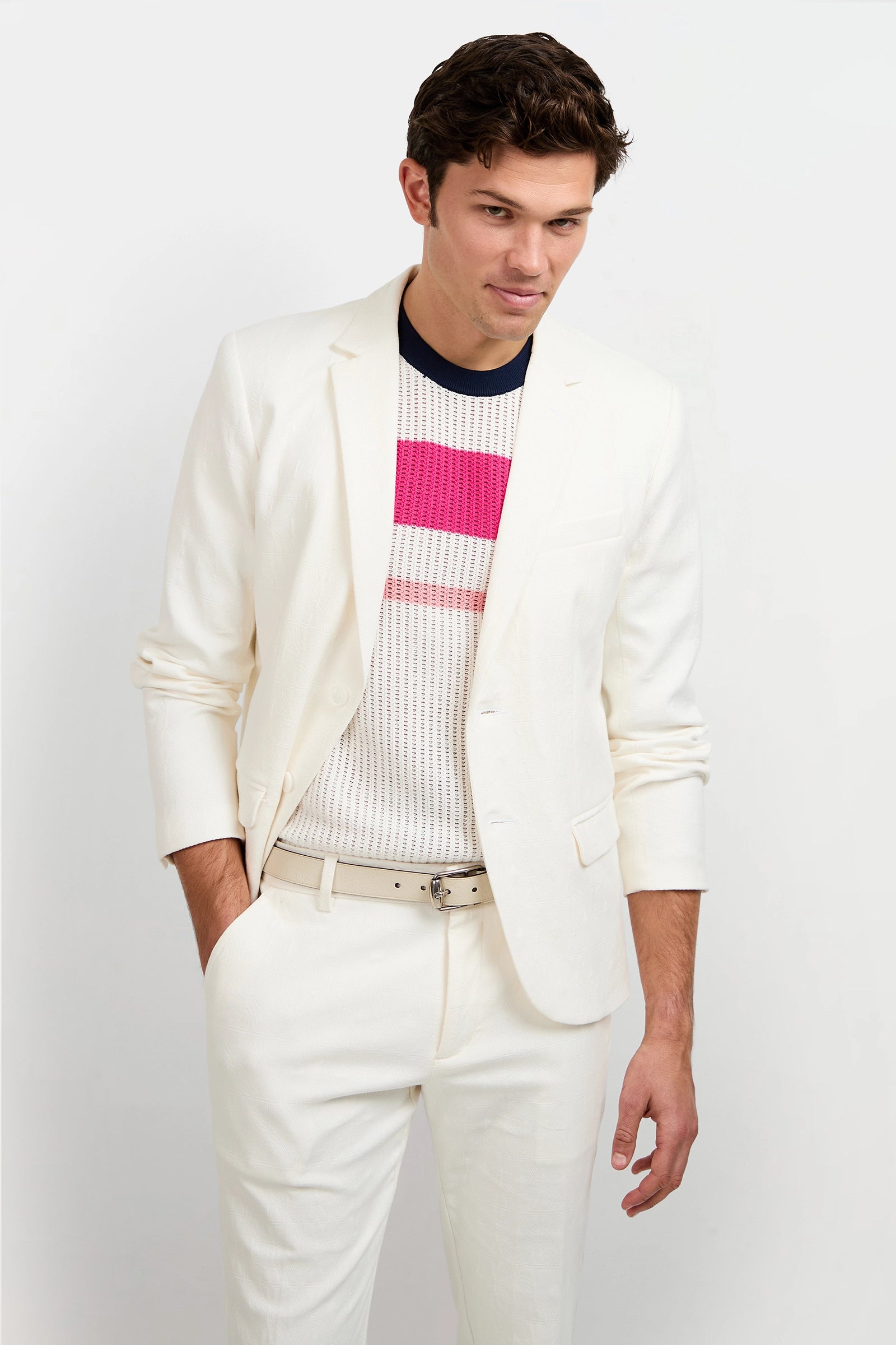 A man wearing the Thurston Blazer - Tegola Textured Jacquard stands against a plain white background, looking slightly down with one hand in his pocket.