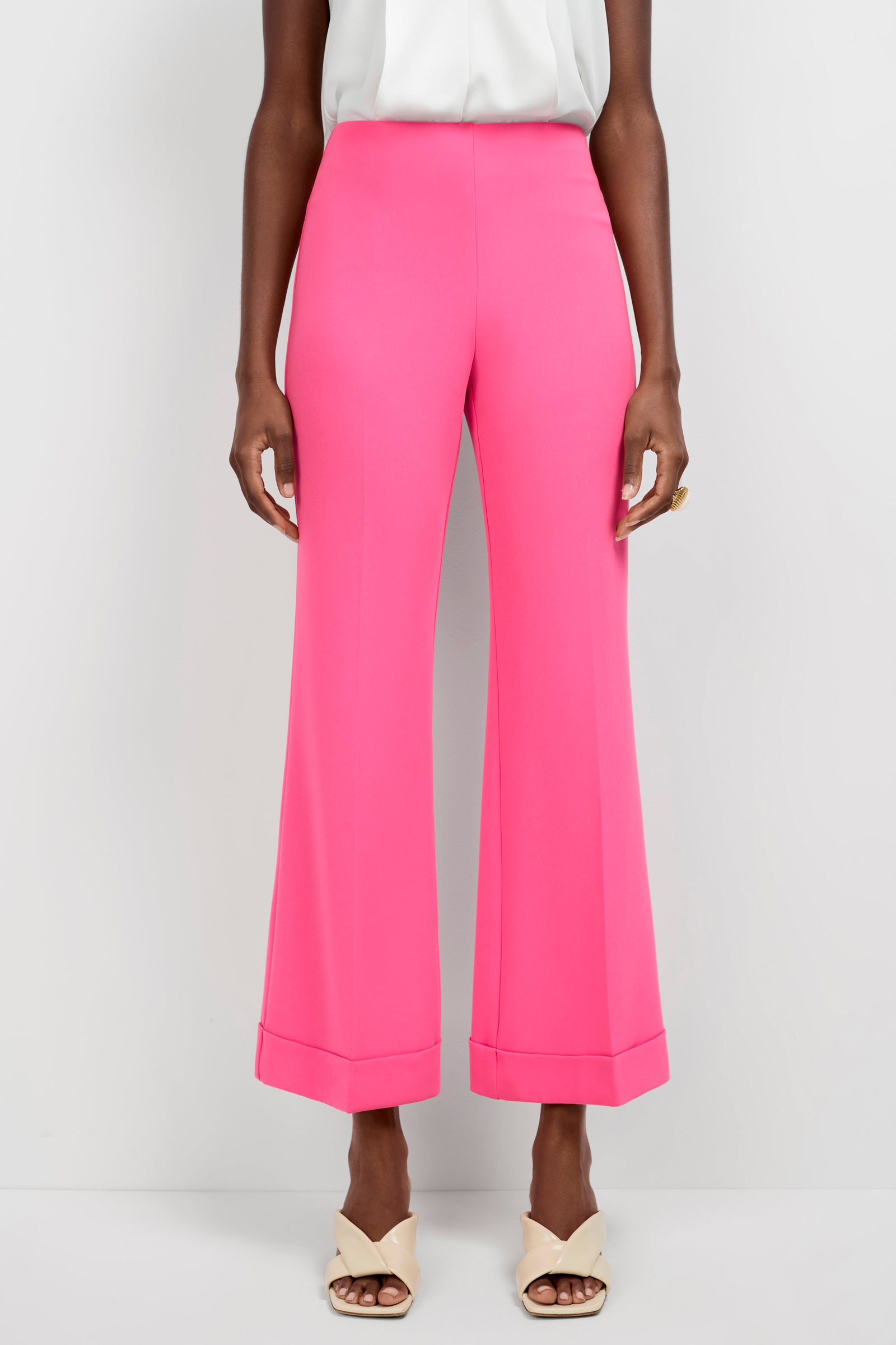 A person wearing bright pink Loren Cropped Kick-Flare Pants, a white sleeveless top, cream heeled sandals, and a gold ring stands against a plain white background.