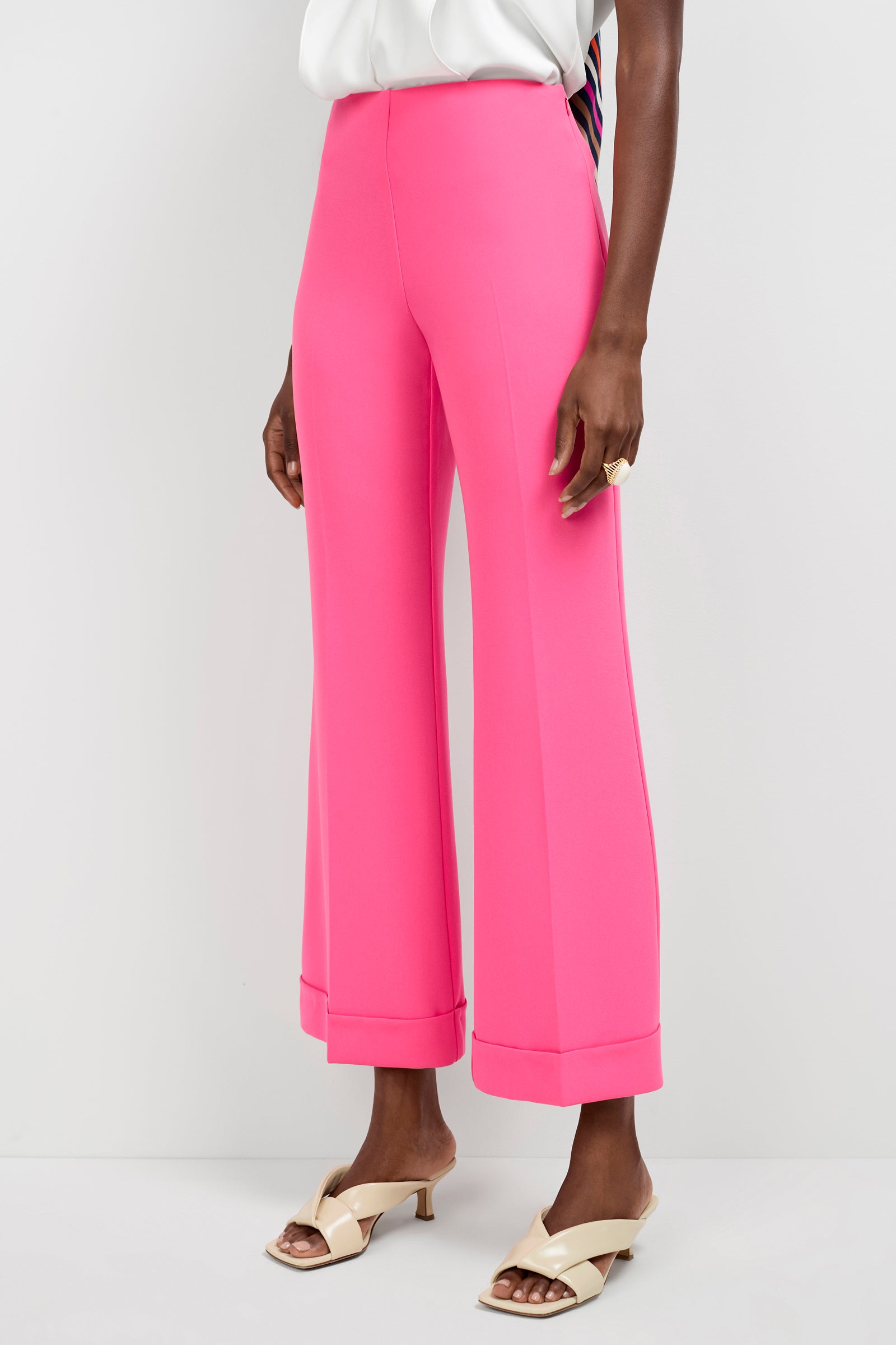 A person stands against a plain white background wearing bright pink Loren Cropped Kick-Flare Pants, cream heeled sandals, a white top, and a gold ring.