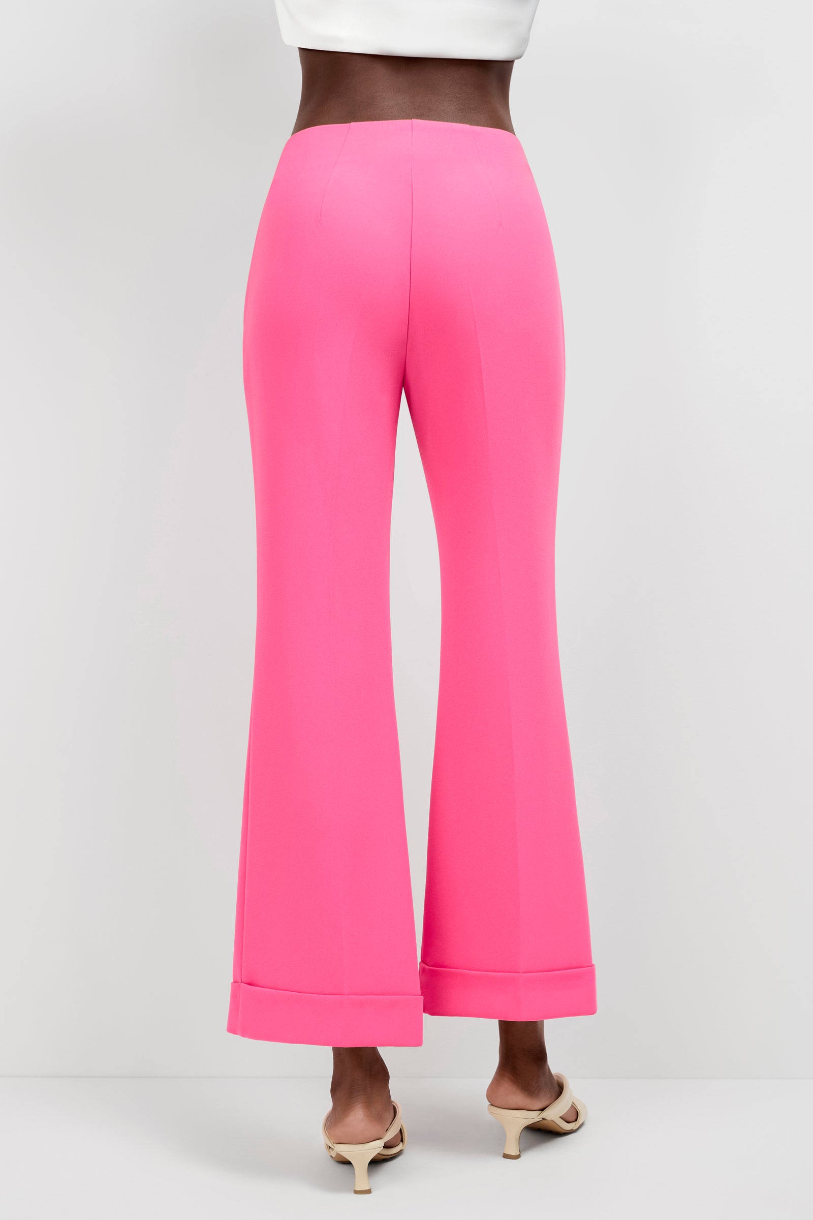 A person wearing Loren Cropped Kick-Flare Pants in bright pink, paired with cream heeled sandals, stands against a plain white background. Only the lower torso and legs are visible.