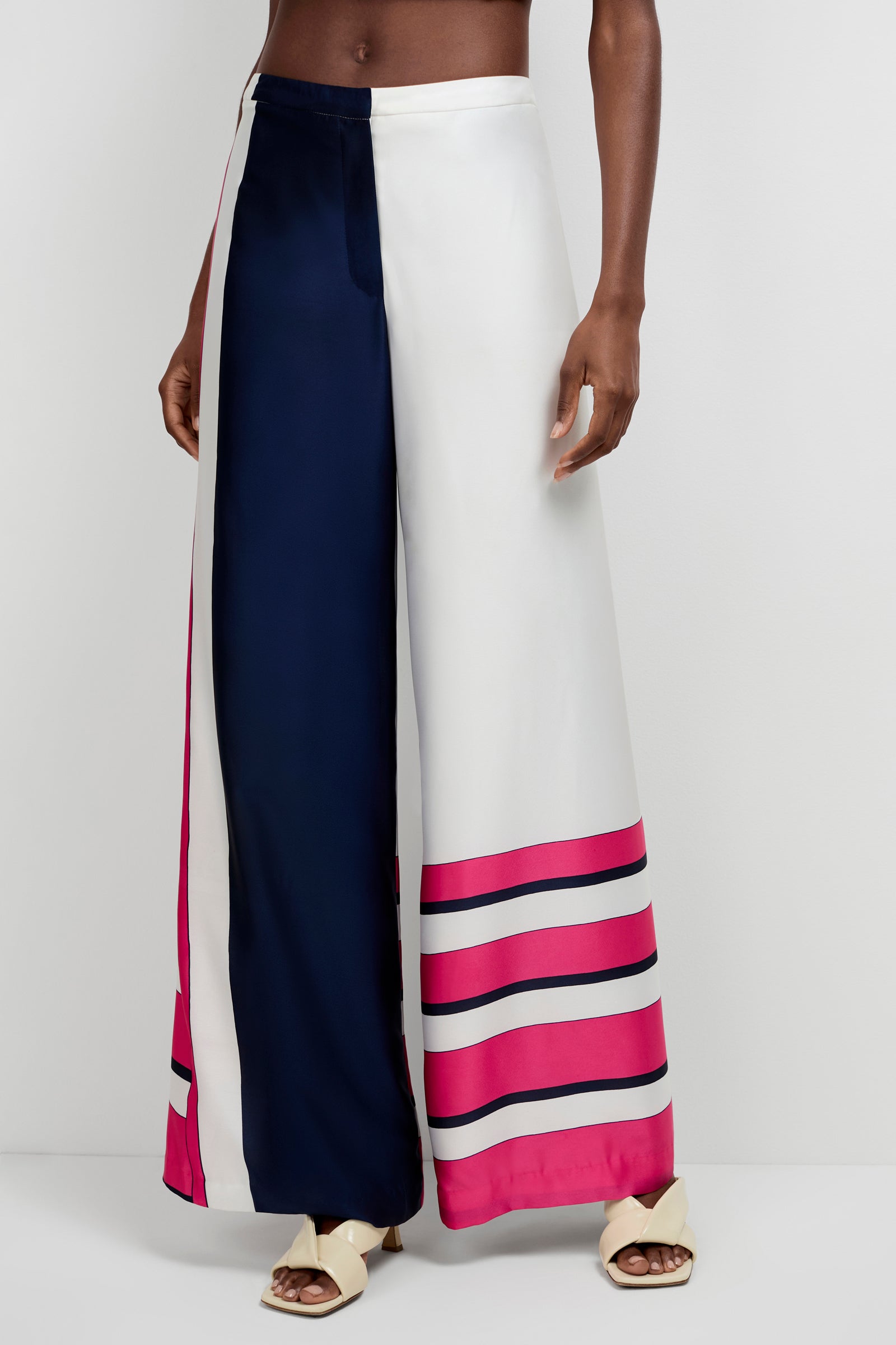 Someone in the Lanay Linee Wide-Leg Panta, featuring high-waisted, wide-leg styling and a navy, white, pink, and magenta color-block stripe pattern, paired with cream open-toe sandals.
