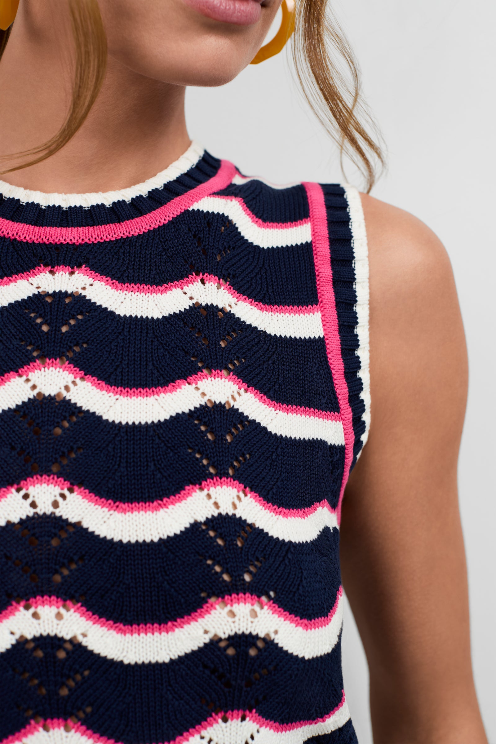 Close-up of a person with light brown skin wearing the Cawley Knit Tank, featuring navy blue, white, and pink wavy stripes. The image shows the shoulders up.