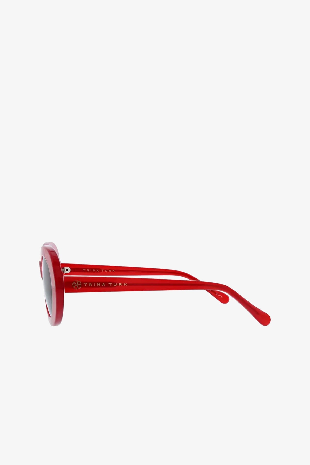 Side view of Carova Oval Sunglasses with red round frames and dark lenses, featuring TRINA TURK branding on the arm, displayed against a plain white background.