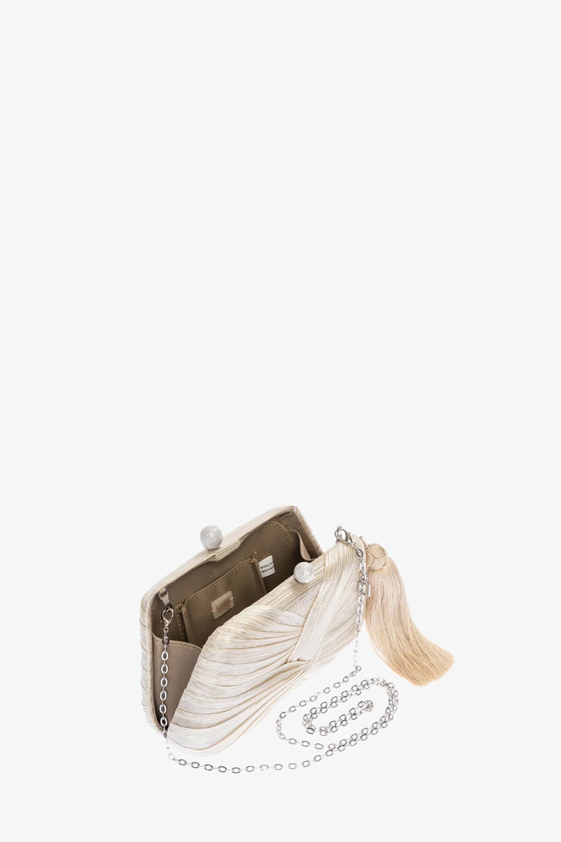 The Rosie Draped Clutch is a small, elegant beige purse with a wavy texture, metal clasp, long silver chain strap, and large beige tassel. Opened, it reveals a tan interior with pockets.