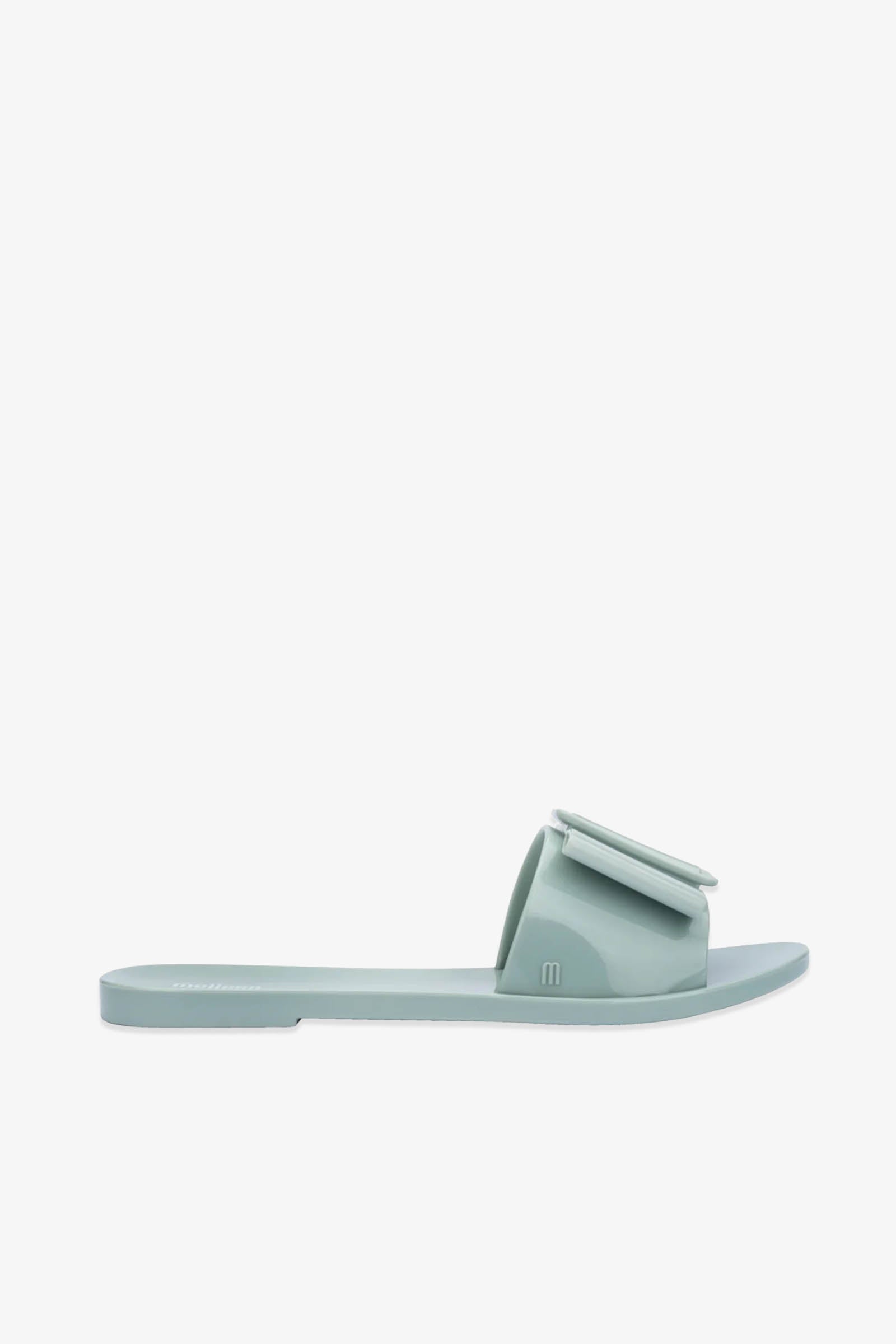Introducing the Babe Sandals: stylish light green slide sandals with a flat sole and a wide strap across the top, highlighted by a charming decorative bow detail. Set against a plain white background.