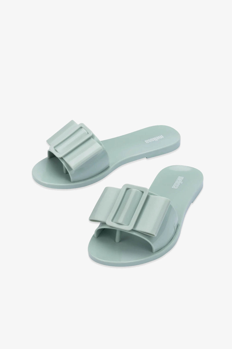 A pair of Babe Sandals in light green, featuring large decorative bows on the straps, displayed against a white background.