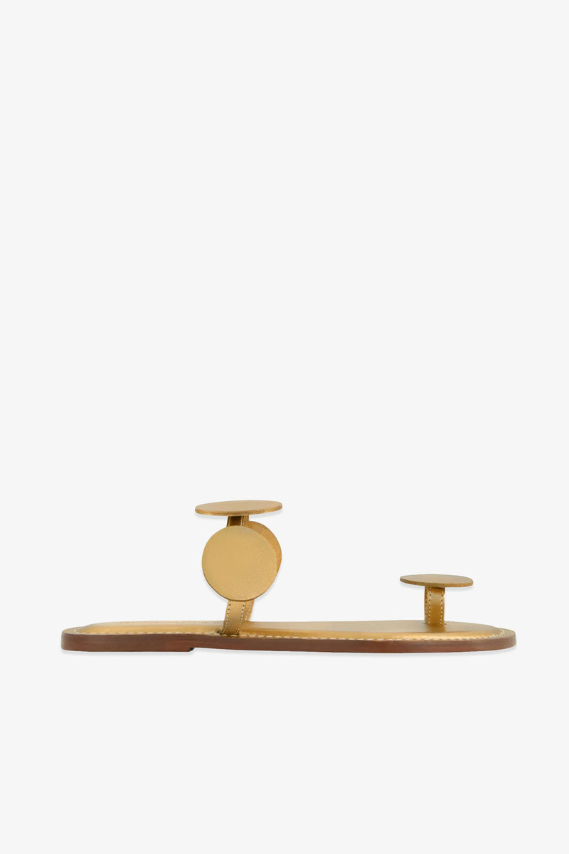 The New Moon Sandal features a gold flat design with two circular straps—one over the toe and one across the midfoot—set on a thin brown sole, and is displayed against a plain white background.