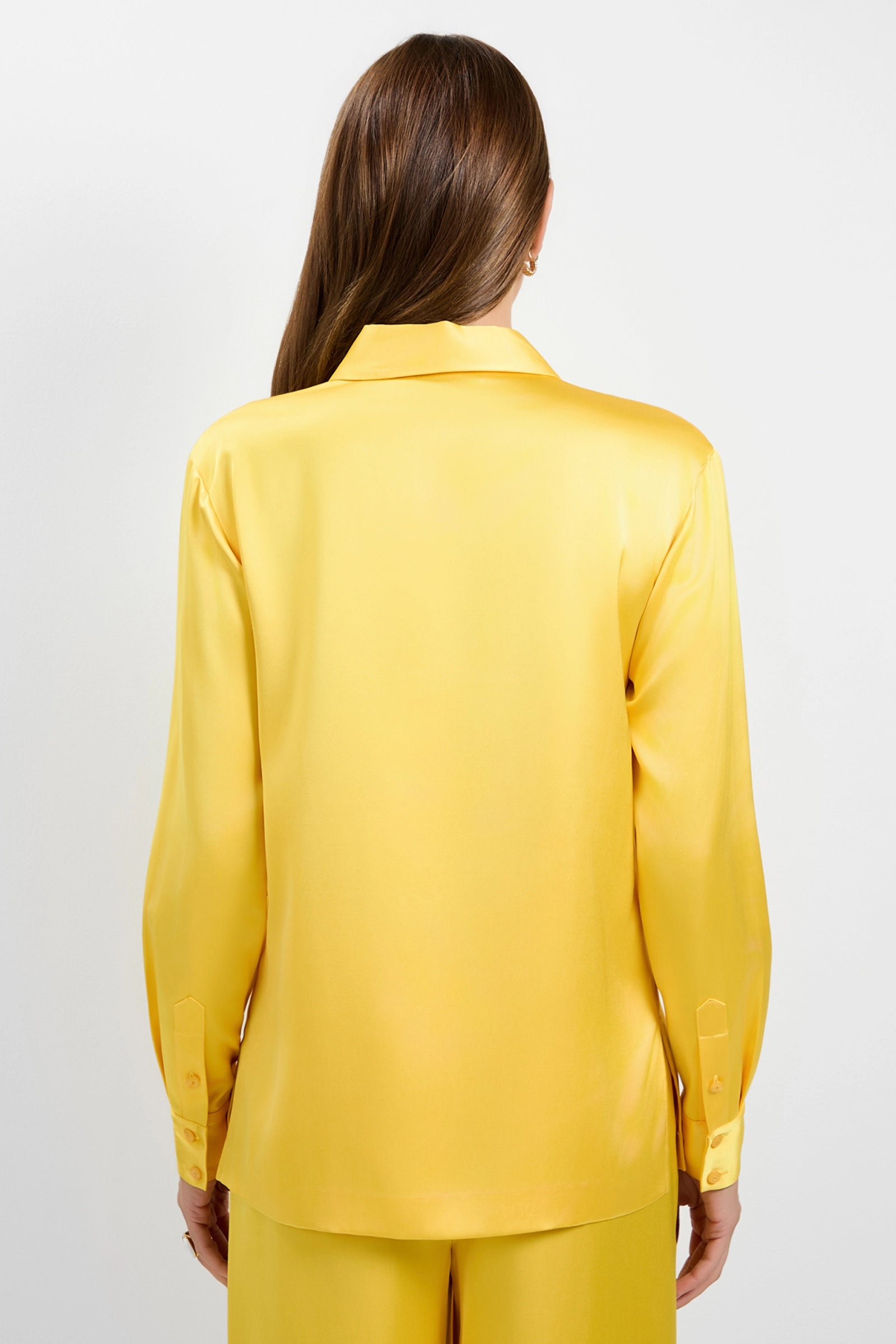 A person with long brown hair, seen from behind, is wearing the Bristlecone Satin Shirt in bright yellow with long sleeves and matching yellow pants against a plain white background.