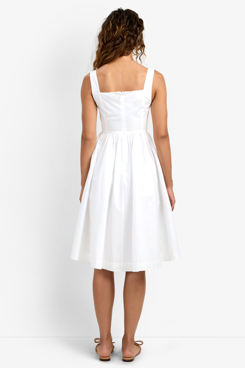 Woman with long curly hair, seen from behind, models the Mirabello Sweetheart Neck Midi Dress in white against a plain background. She wears sandals and the dress is sleeveless and knee-length.