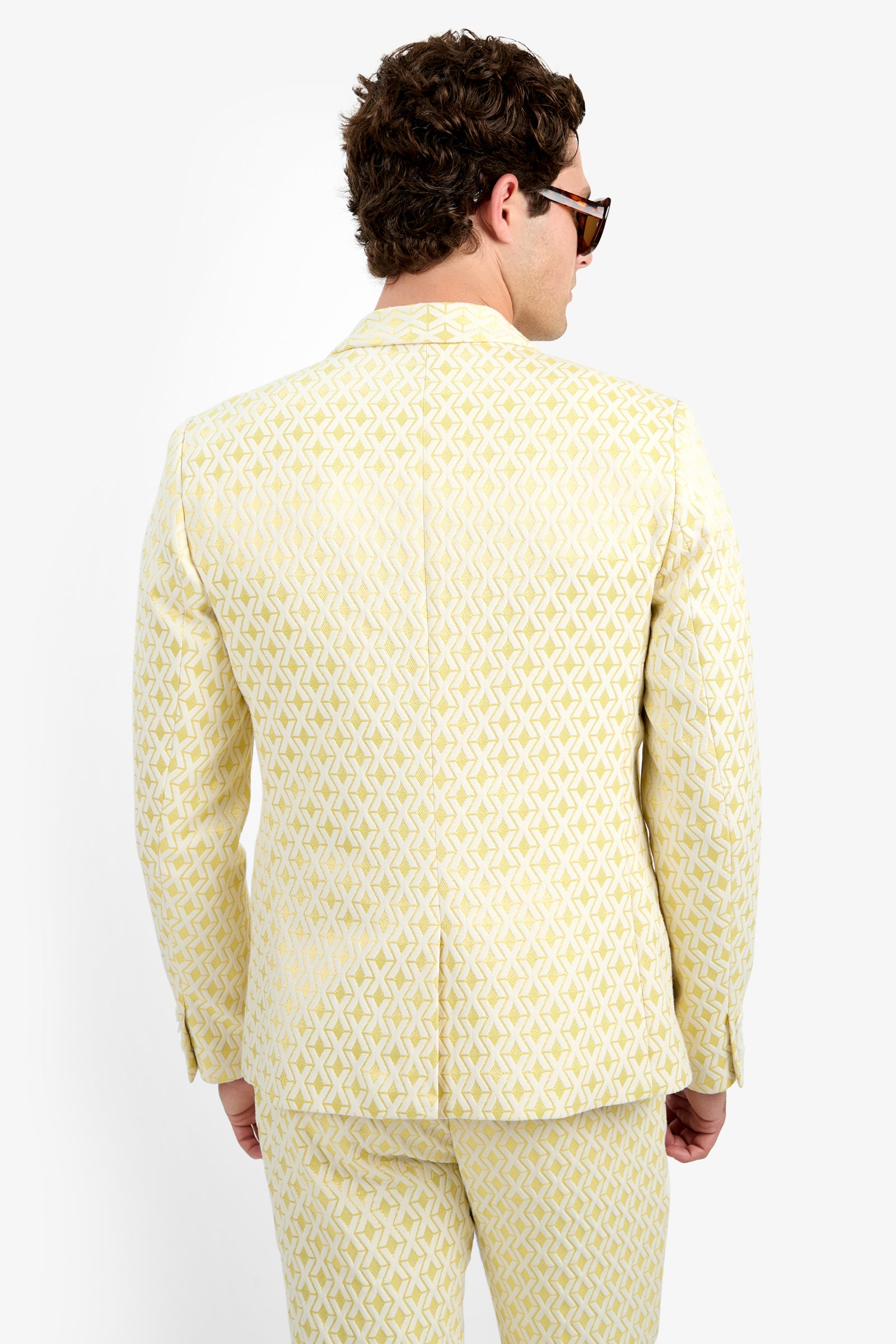 A man with curly brown hair, sunglasses, and the Thurston Blazer - Crossroads Jacquard stands with his back to the camera against a plain white background.