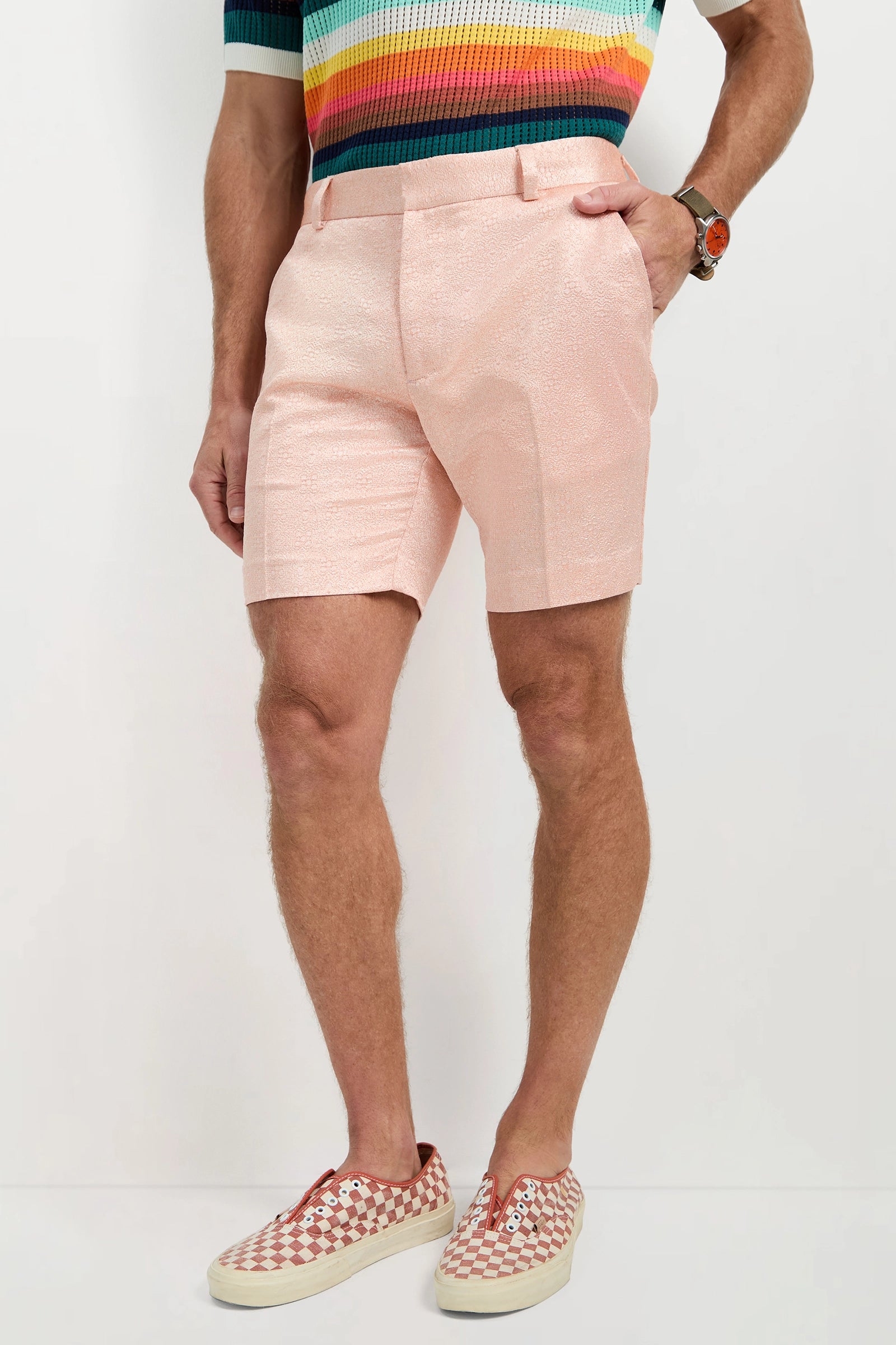 A person wearing the Clyde Short - Metallic Jacquard, a colorful striped knit shirt, patterned slip-on shoes, and a wristwatch stands against a plain white background.