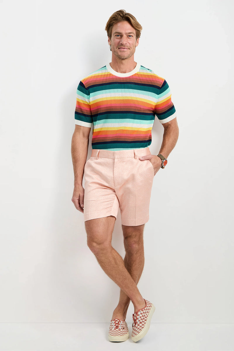 A man poses against a white wall wearing the Clyde Short - Metallic Jacquard, pairing it with a colorful striped sweater and slip-on shoes. He smiles with one hand in his pocket and the other relaxed by his side.
