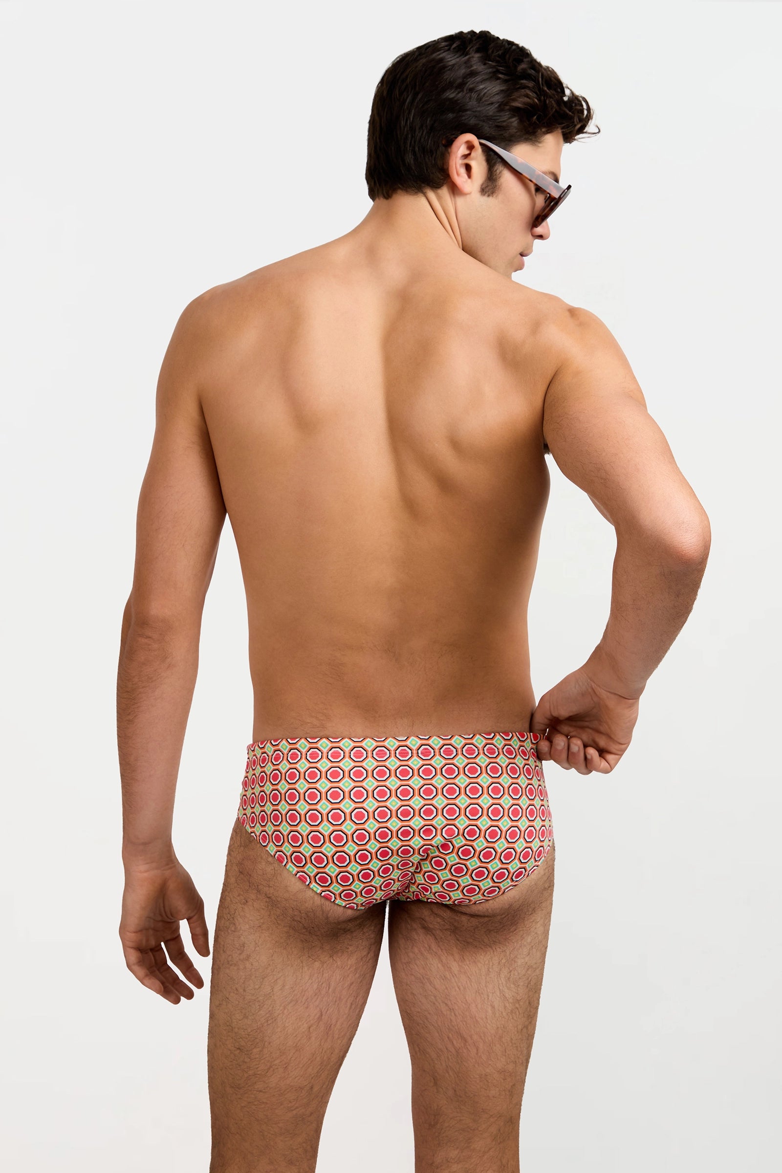 A man with short dark hair and glasses models the Bondi Swim Brief - Salerno, standing with his back to the camera against a plain light background.