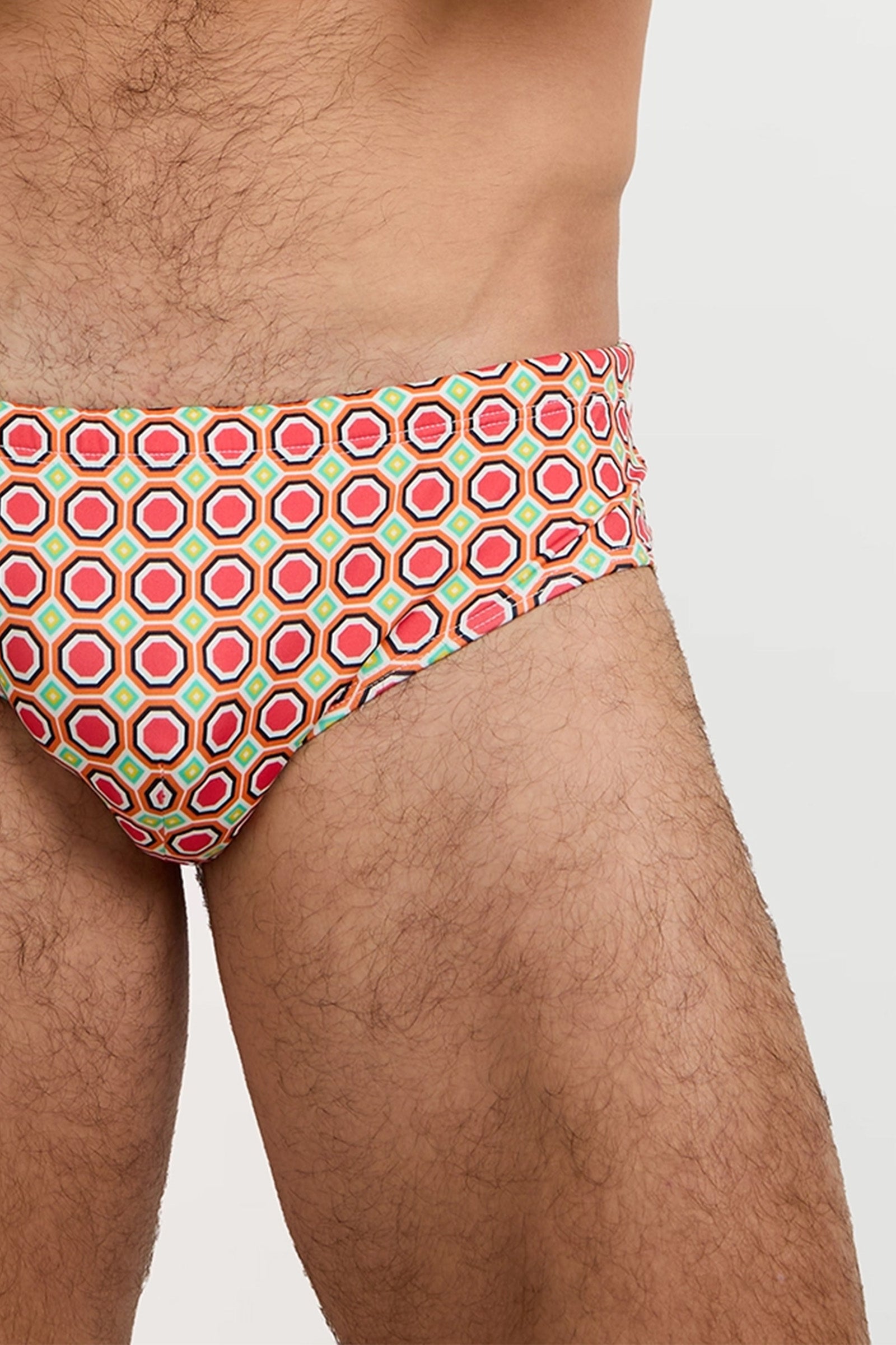 A close-up of a person wearing the Bondi Swim Brief - Salerno, featuring colorful geometric patterns, highlighting their upper thighs and lower torso against a plain background.