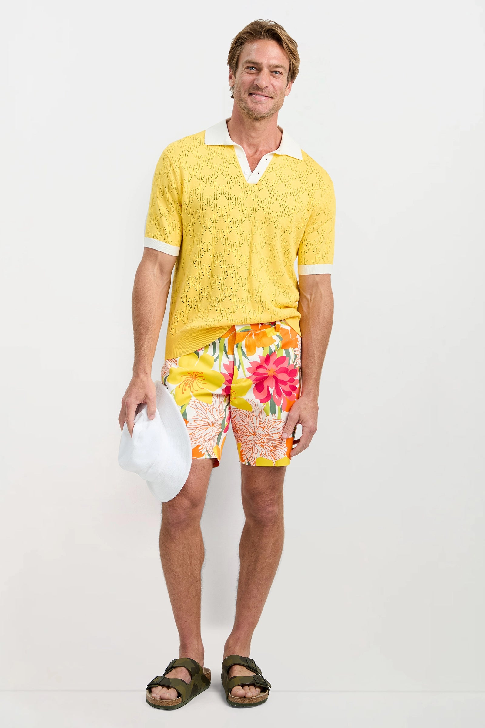 Man wearing a yellow patterned shirt and colorful floral shorts on a white background