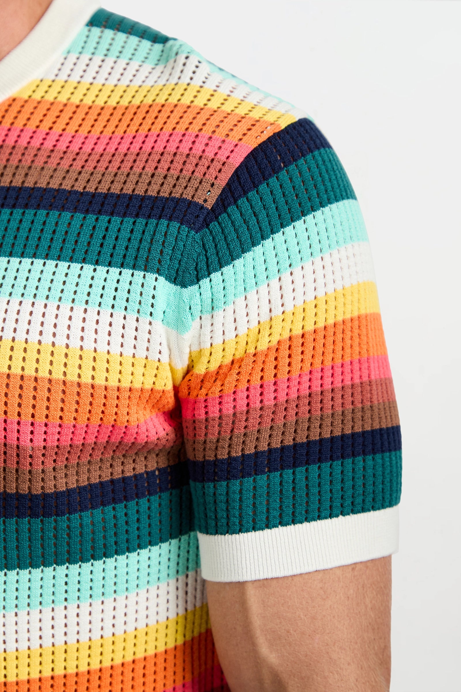 A close-up of a person's upper arm and shoulder wearing the Carlos Short-Sleeve Mesh Crewneck, featuring horizontal rainbow stripes with a white collar and sleeve cuffs.