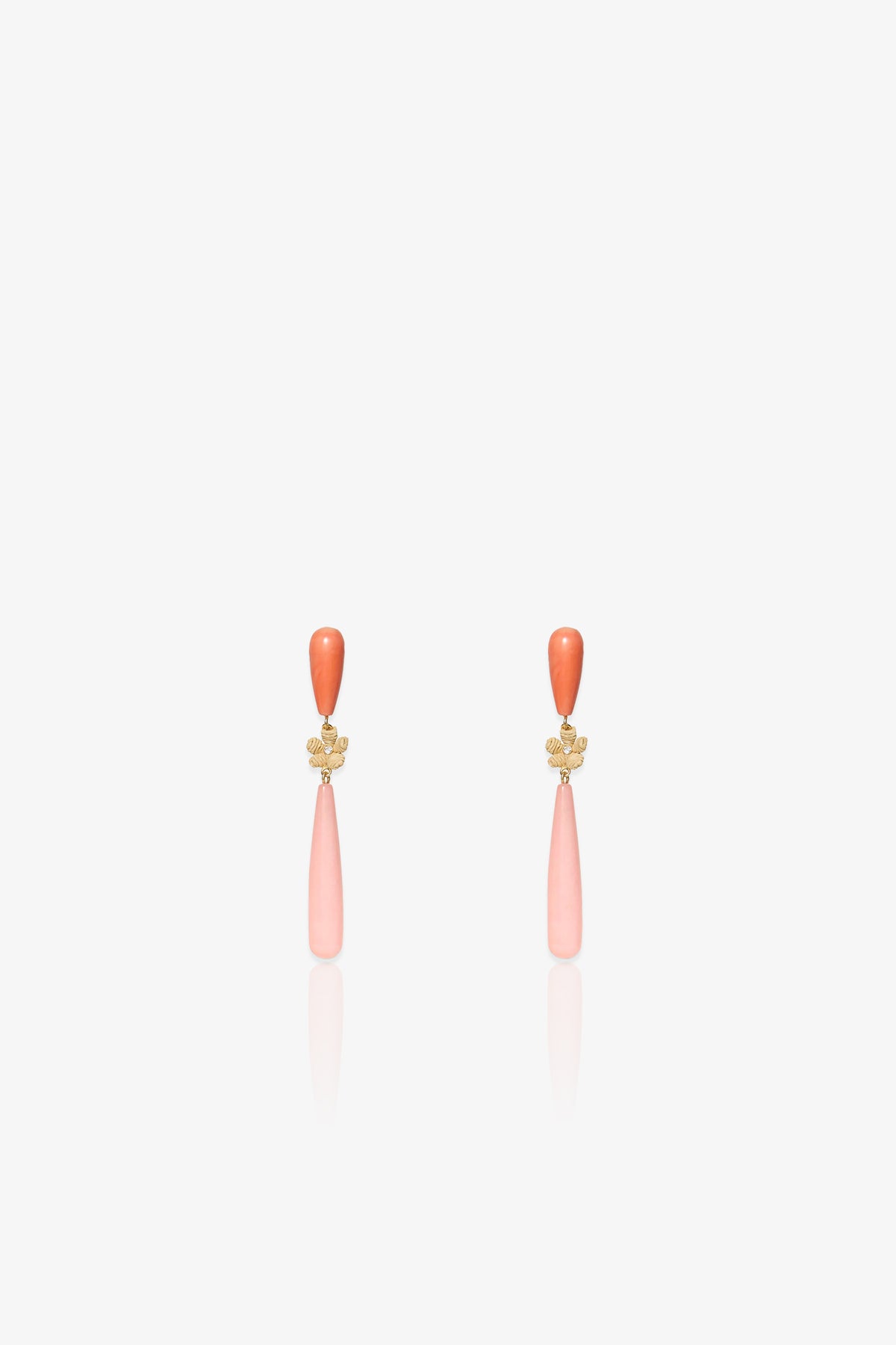 The Flamingo Linear Earring is an elegant pair of drop earrings featuring a small orange bead at the top, a gold floral accent in the middle, and a long, light pink teardrop-shaped pendant hanging below, displayed on a white background.