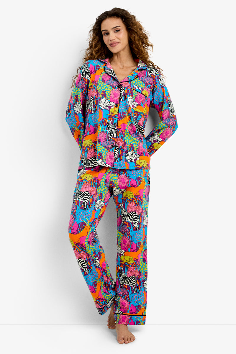 A woman stands barefoot wearing the Classic PJ Set - Jungle, featuring a vibrant jungle-themed pattern with wild animals on a white background.