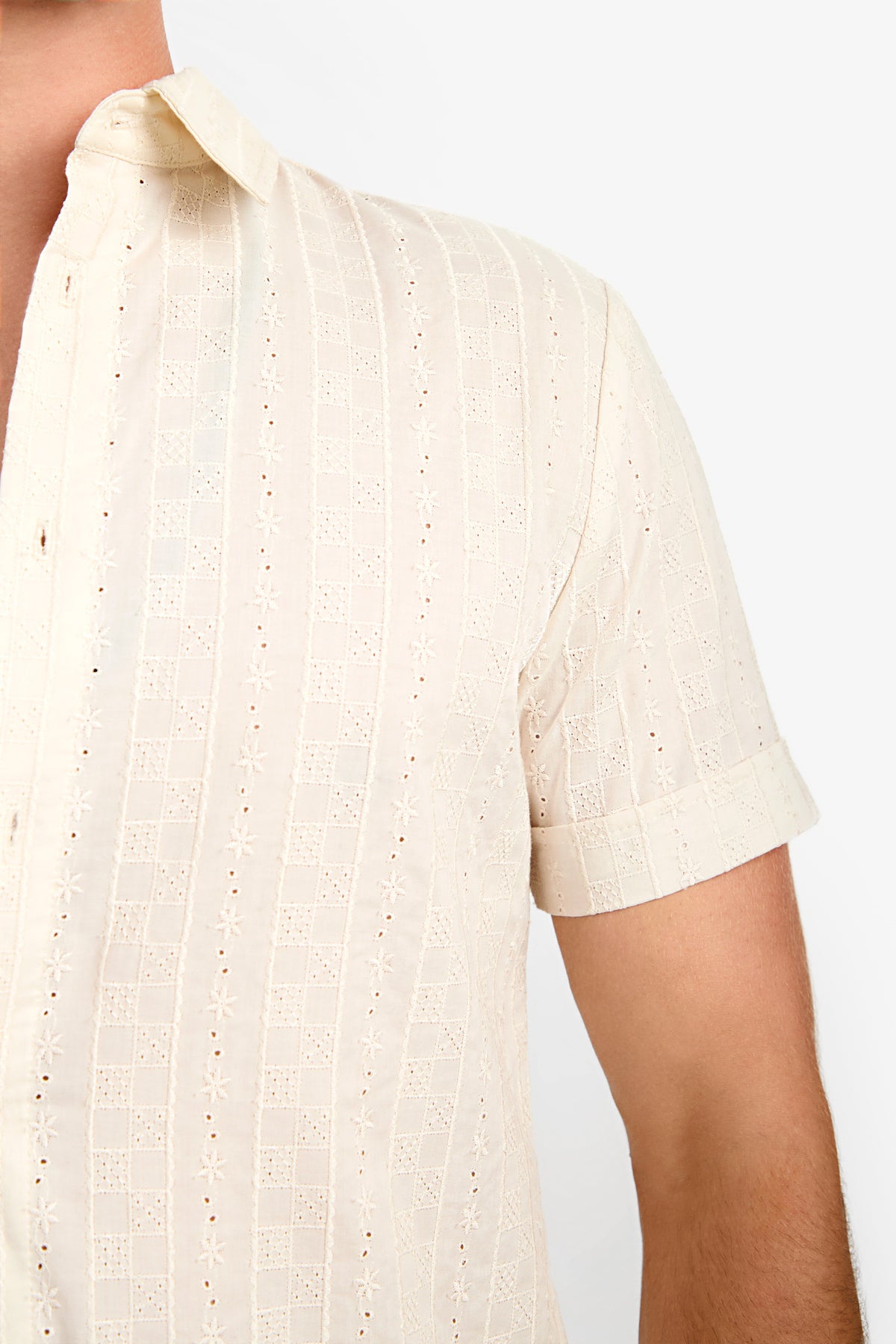 Close-up of a person wearing the Branson Shirt, a short-sleeve, cream-colored patterned button-up with a collar. Only the upper torso and part of the left arm are visible against a plain background.