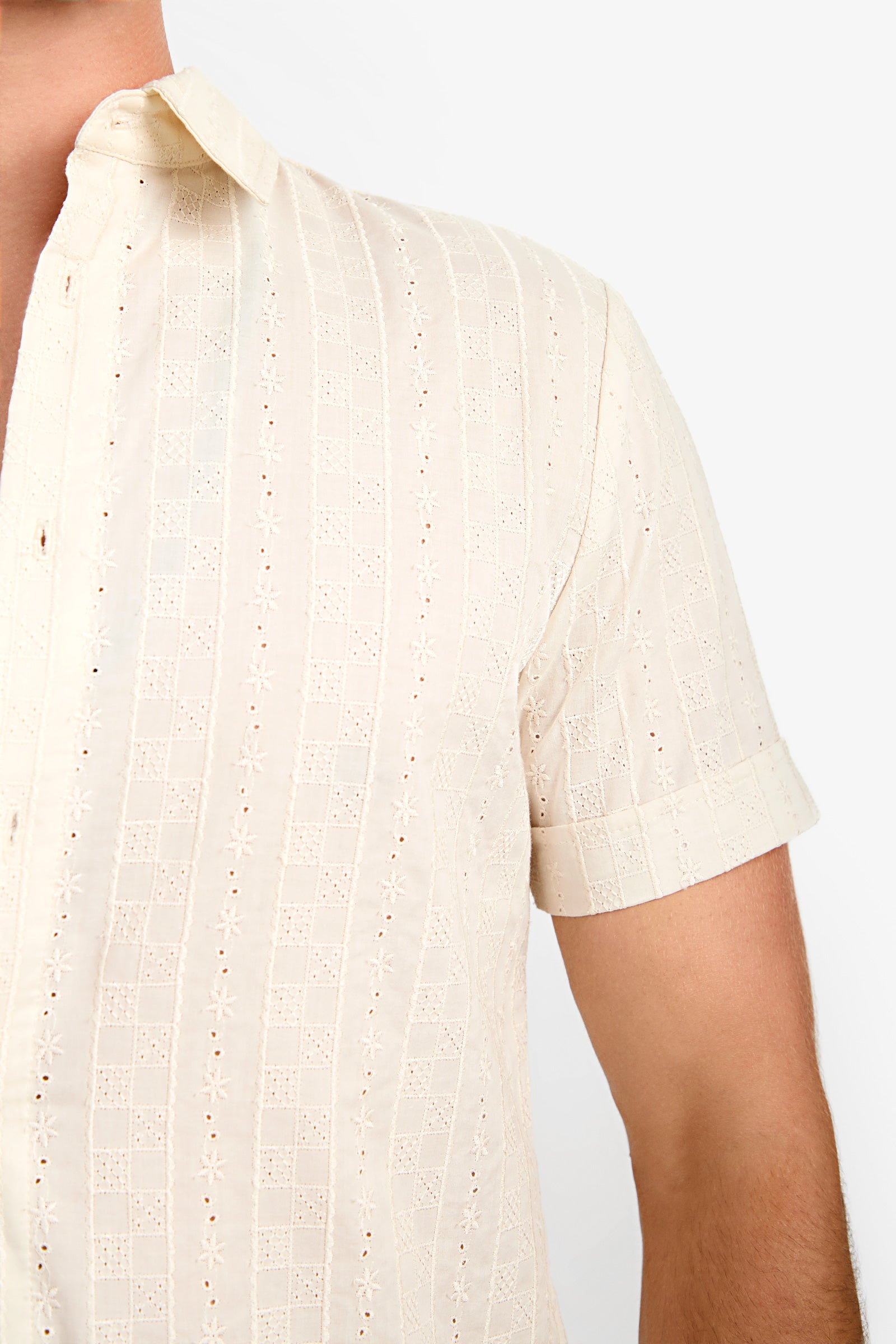 Close-up of a person wearing the Branson Shirt, a short-sleeve, cream-colored patterned button-up with a collar. Only the upper torso and part of the left arm are visible against a plain background.