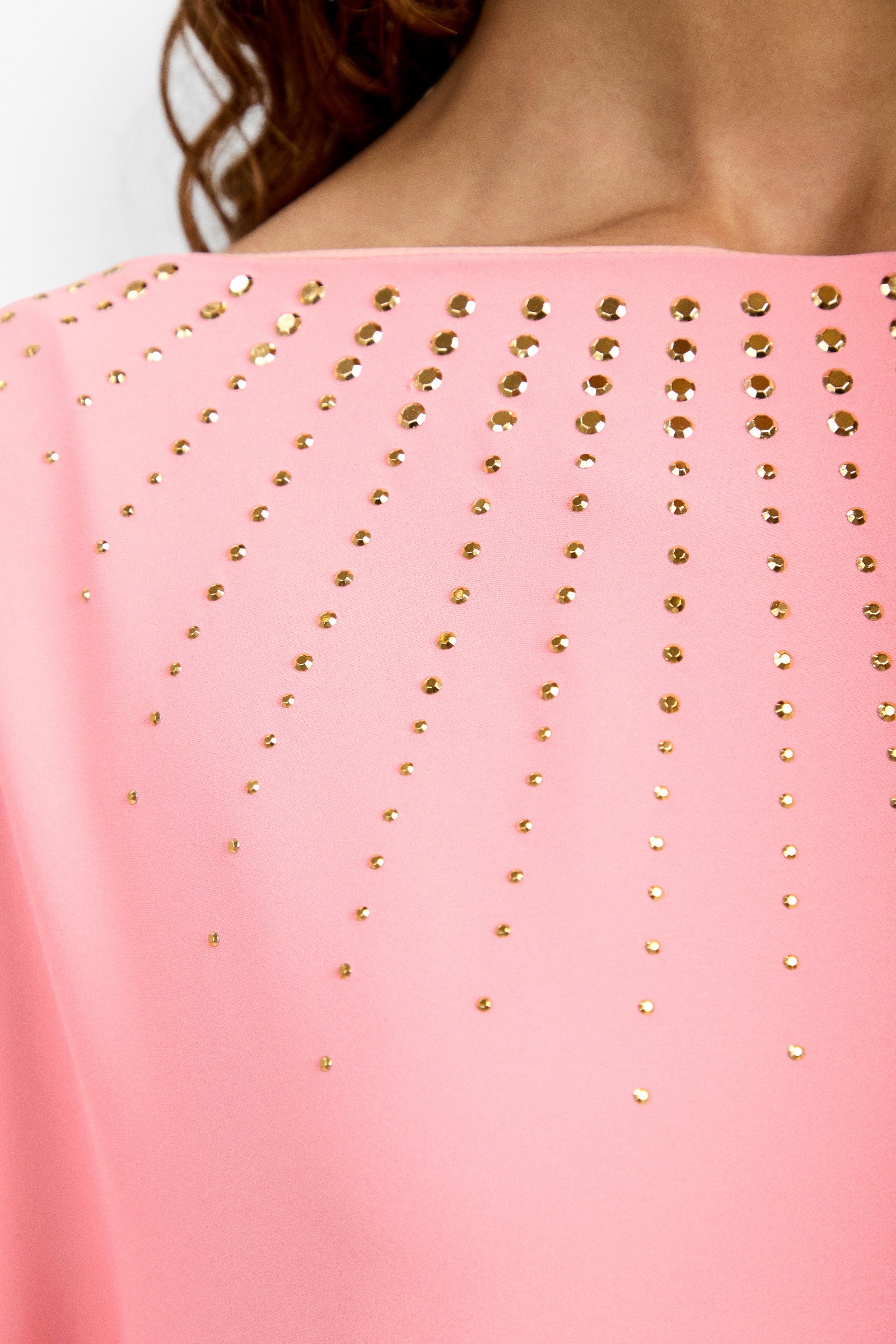 Close-up of the Neena Rhinestone Caftan Dress in pink, featuring gold circular studs in sun ray patterns, worn by a person with light brown skin and partially visible curly hair.