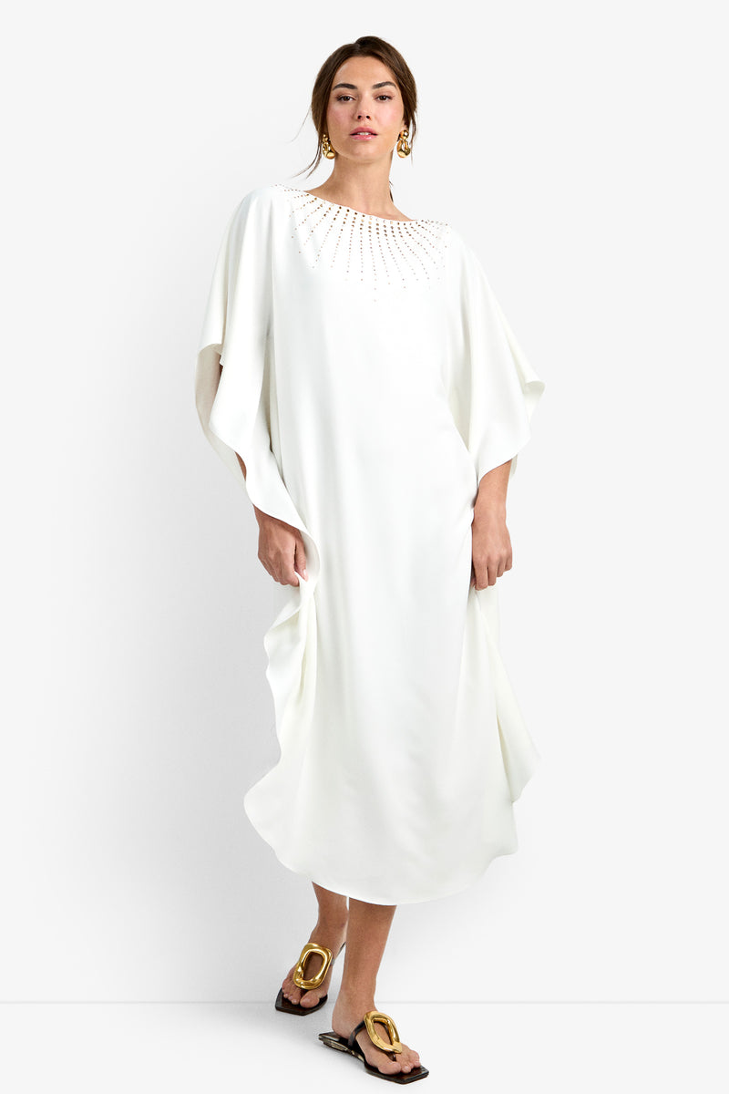 A person wearing the Neena Rhinestone Caftan Dress, gold drop earrings, and gold flat sandals stands against a plain white background.