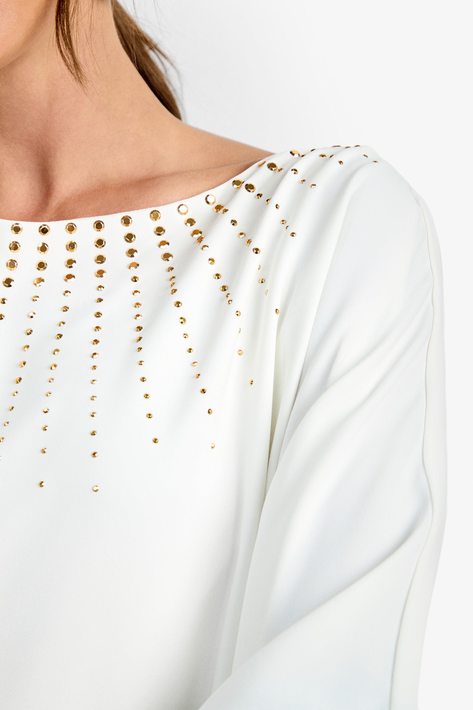 A close-up of a person wearing the Neena Rhinestone Caftan Dress, featuring gold studs radiating from the neckline, with part of their neck, shoulder, and hair visible.