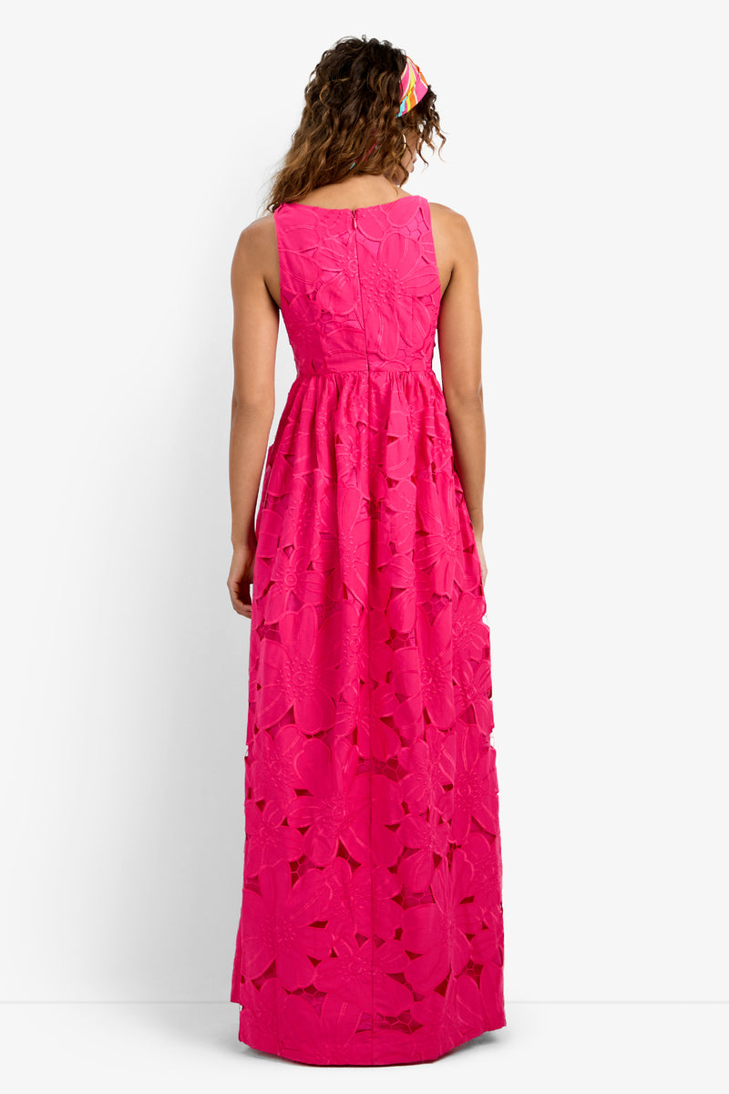 A woman with curly hair, wearing a colorful headband and the Ariel Dress—a sleeveless, bright pink, floor-length dress with a floral cutout pattern—is shown from the back against a white background.
