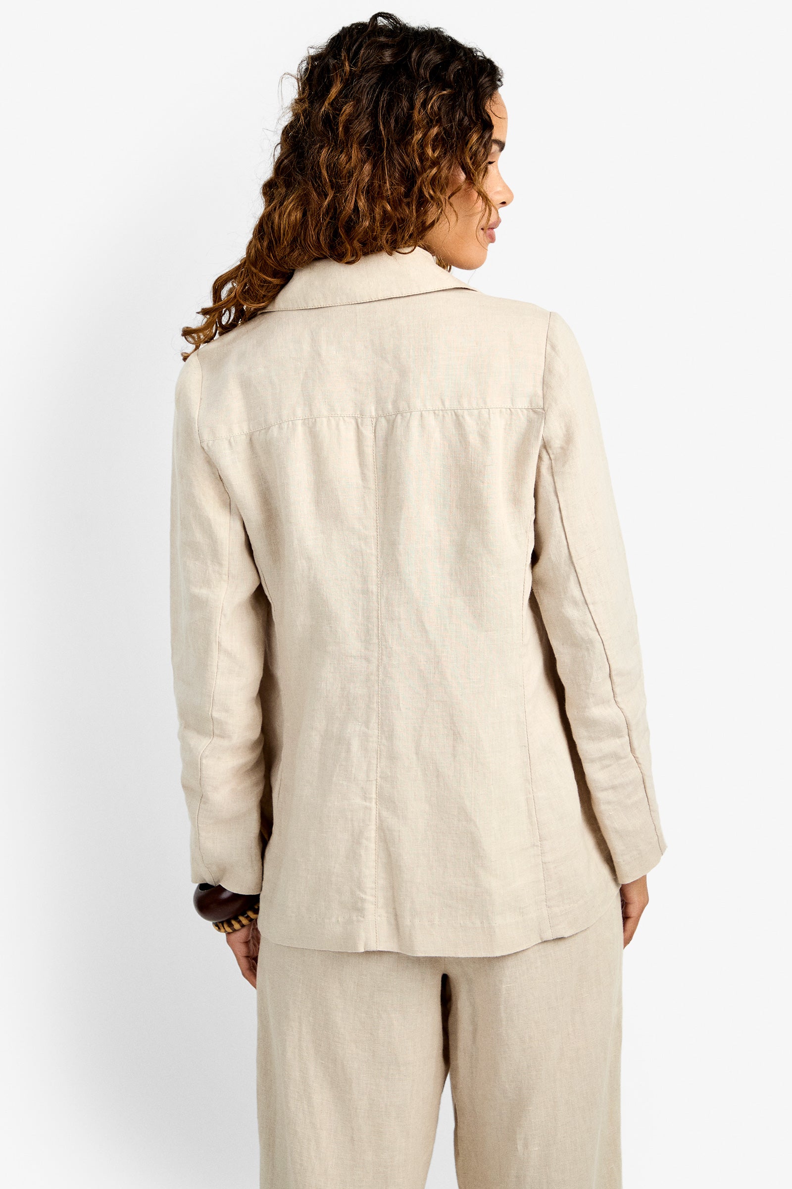 A person with curly hair is shown from the back, wearing the Azurine Blazer and matching pants in light beige linen, set against a plain white background.
