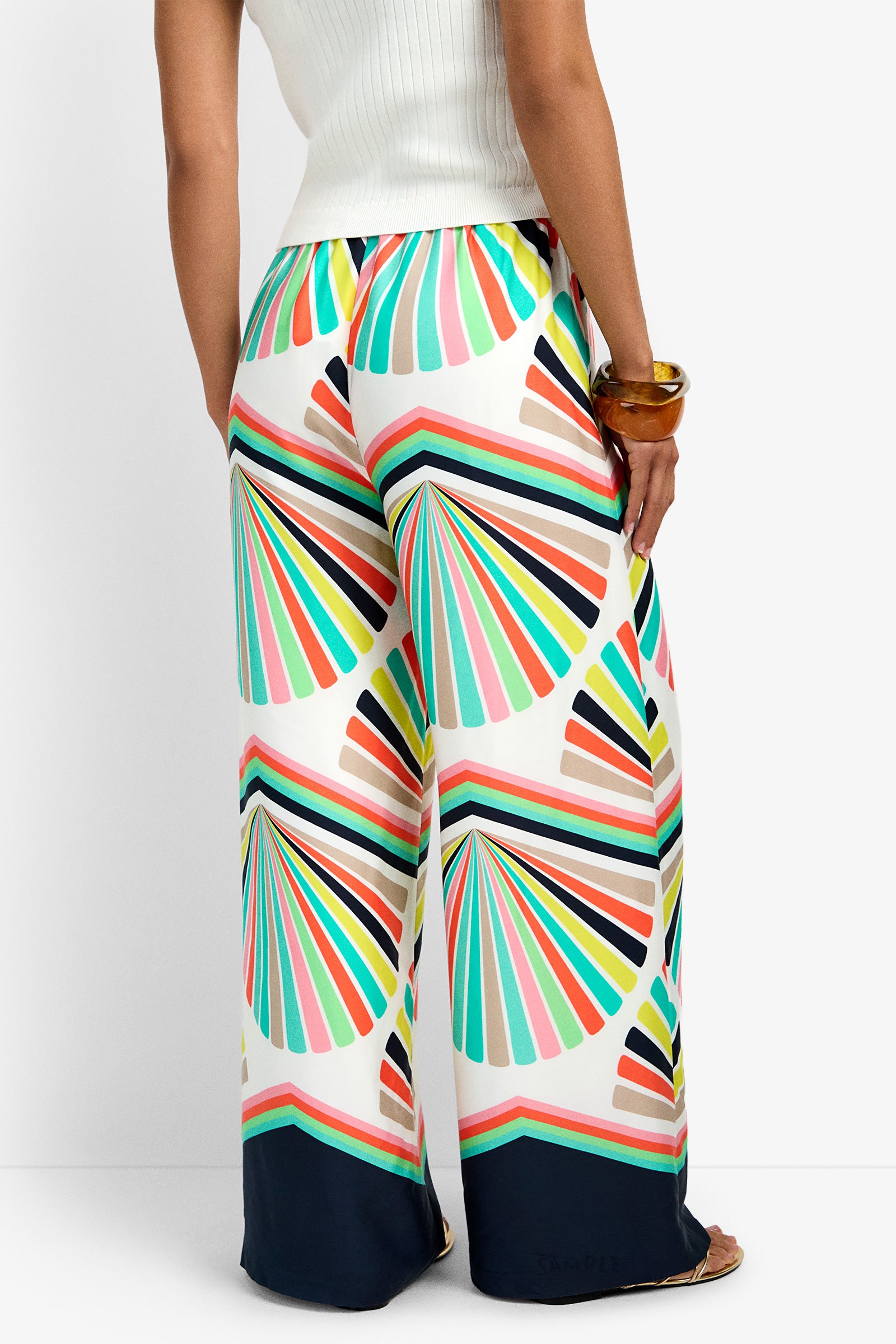 Someone wearing the Dellmar Pant, featuring a colorful geometric fan pattern in pink, green, blue, yellow, and black with a dark navy hem, paired with a white ribbed top.